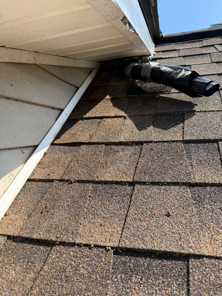 Damaged roof vent and flashing near the eaves with shingles and exposed black ducting