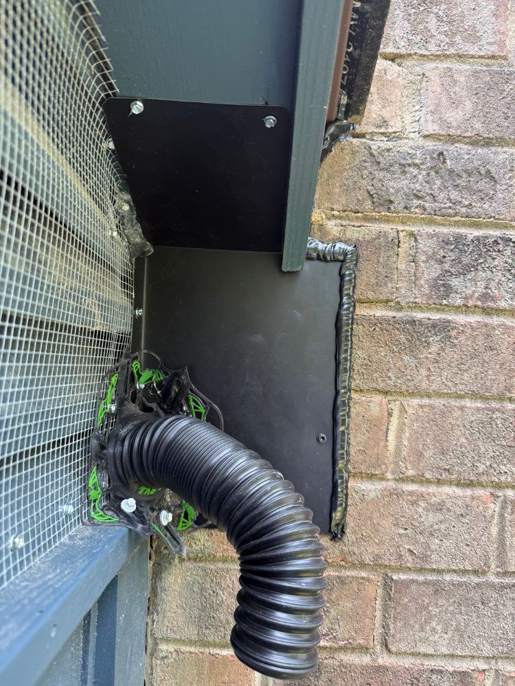 Black drainage pipe beside a wire mesh fence and brick wall, with a metal panel behind it.