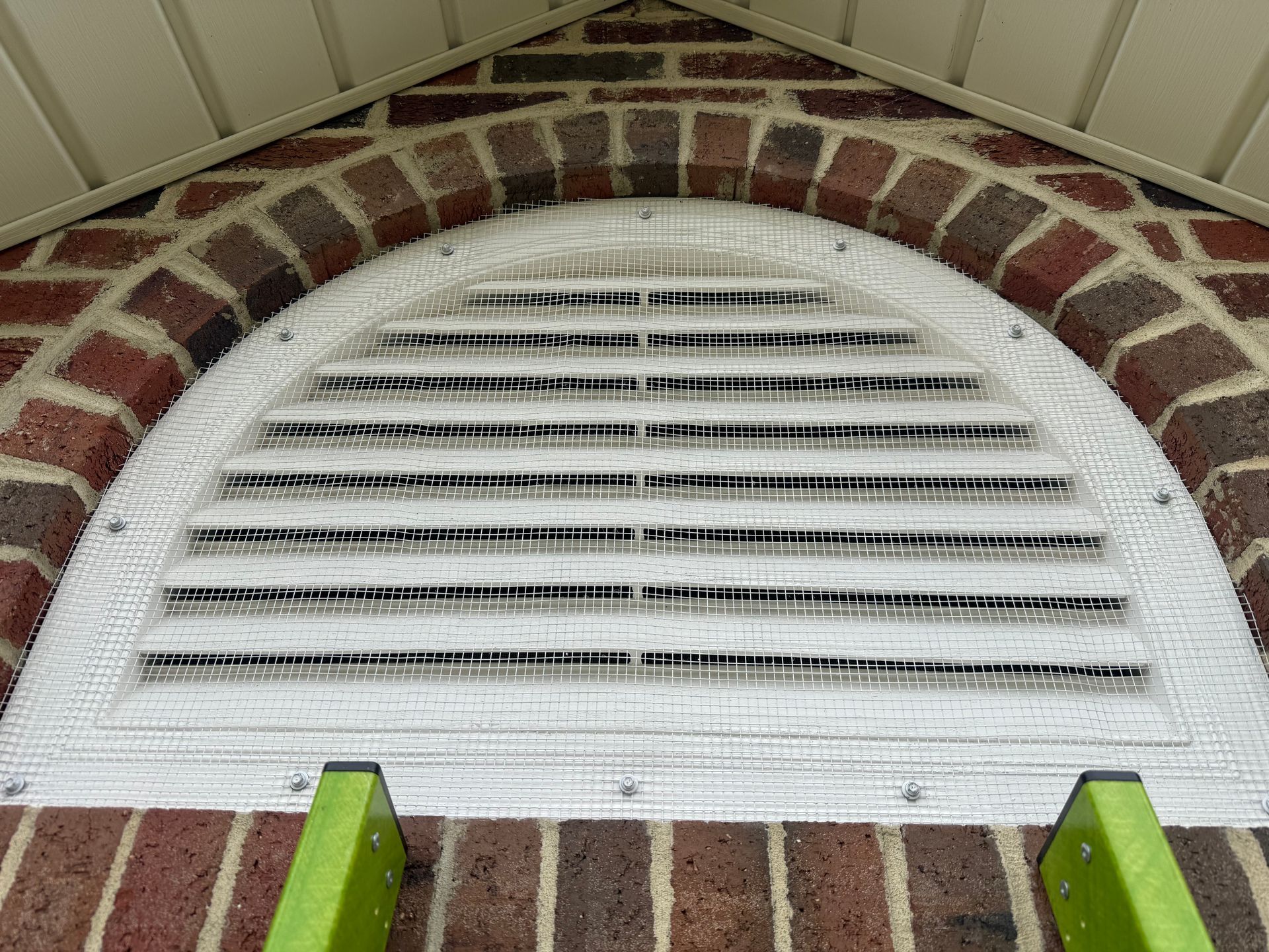 White semicircular window vent in a brick wall with green trim below a beige soffit.