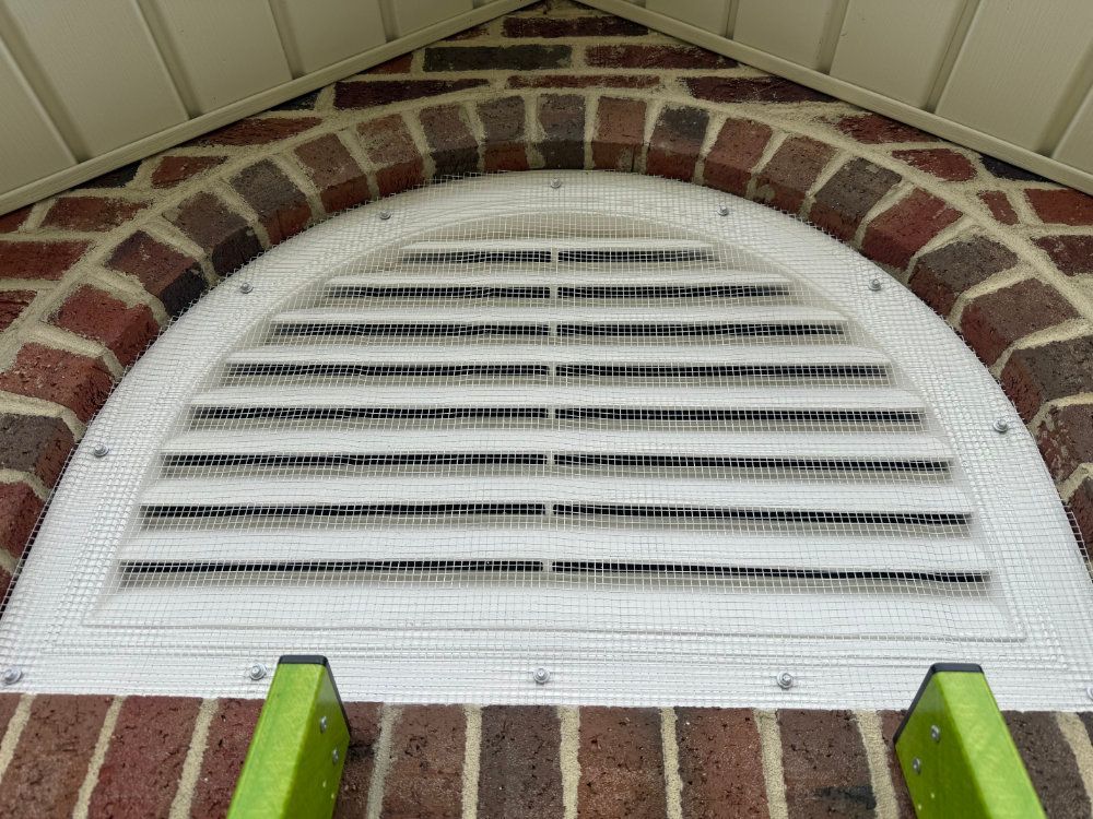 White arched louvered vent set in a brick wall under a roof eave, with green trim below