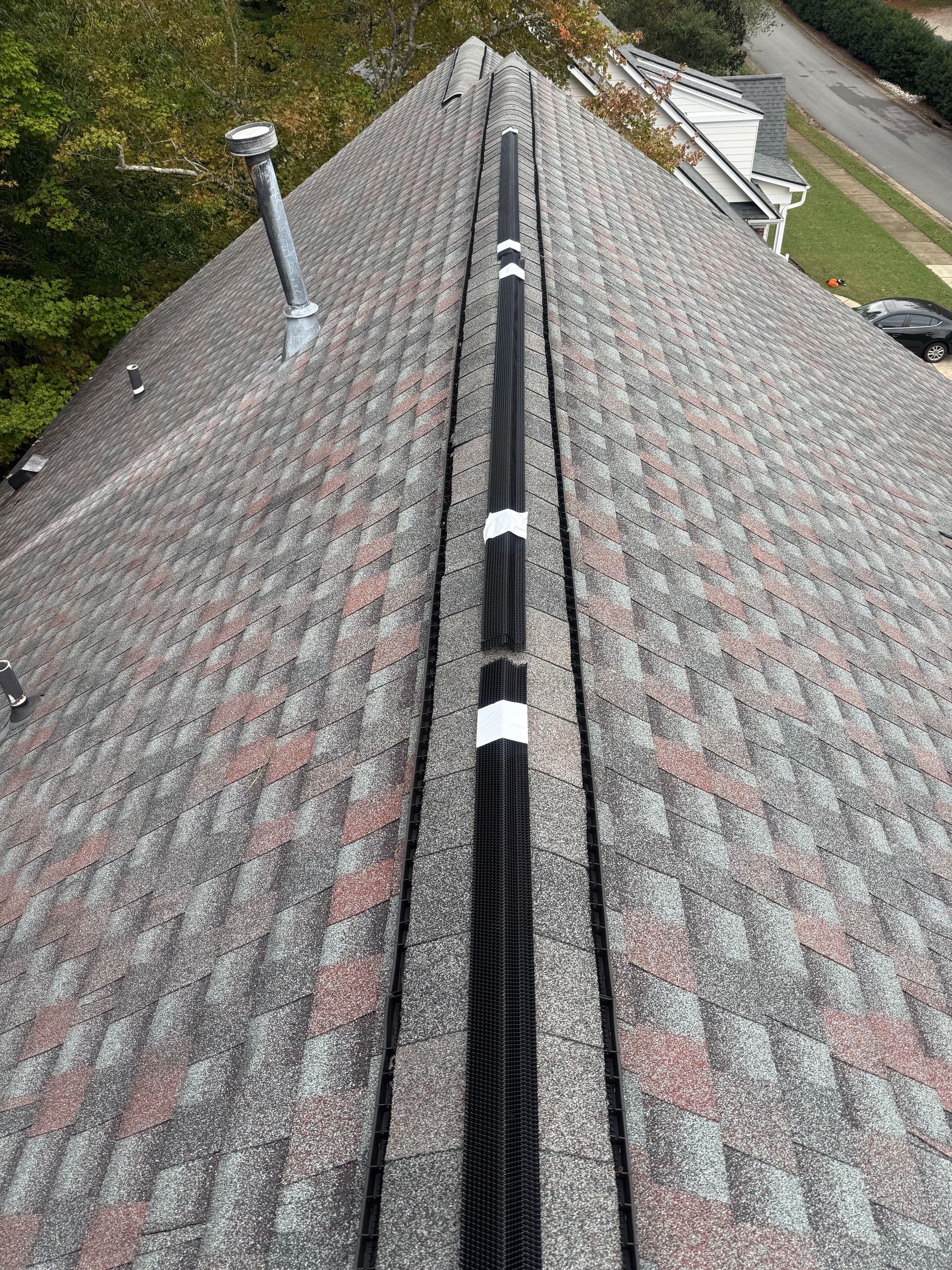 Roof ridge with black vent strip and white fasteners on gray shingle roof, seen from above