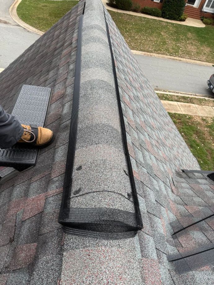Roof ridge with dark shingles and a worker’s boot on the left, viewed from above.