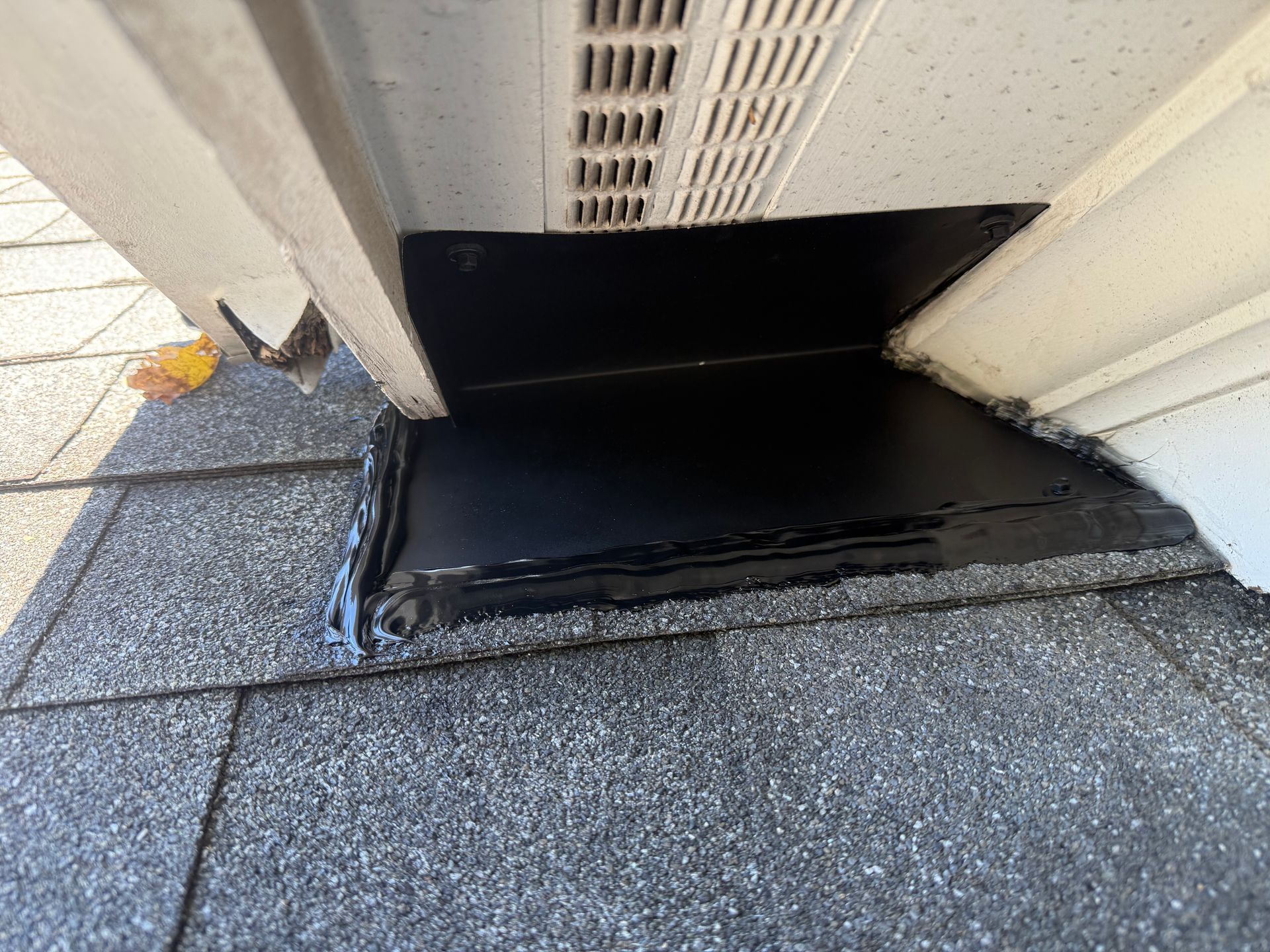 Black roof vent flashing on a gray shingled roof beside a beige wall