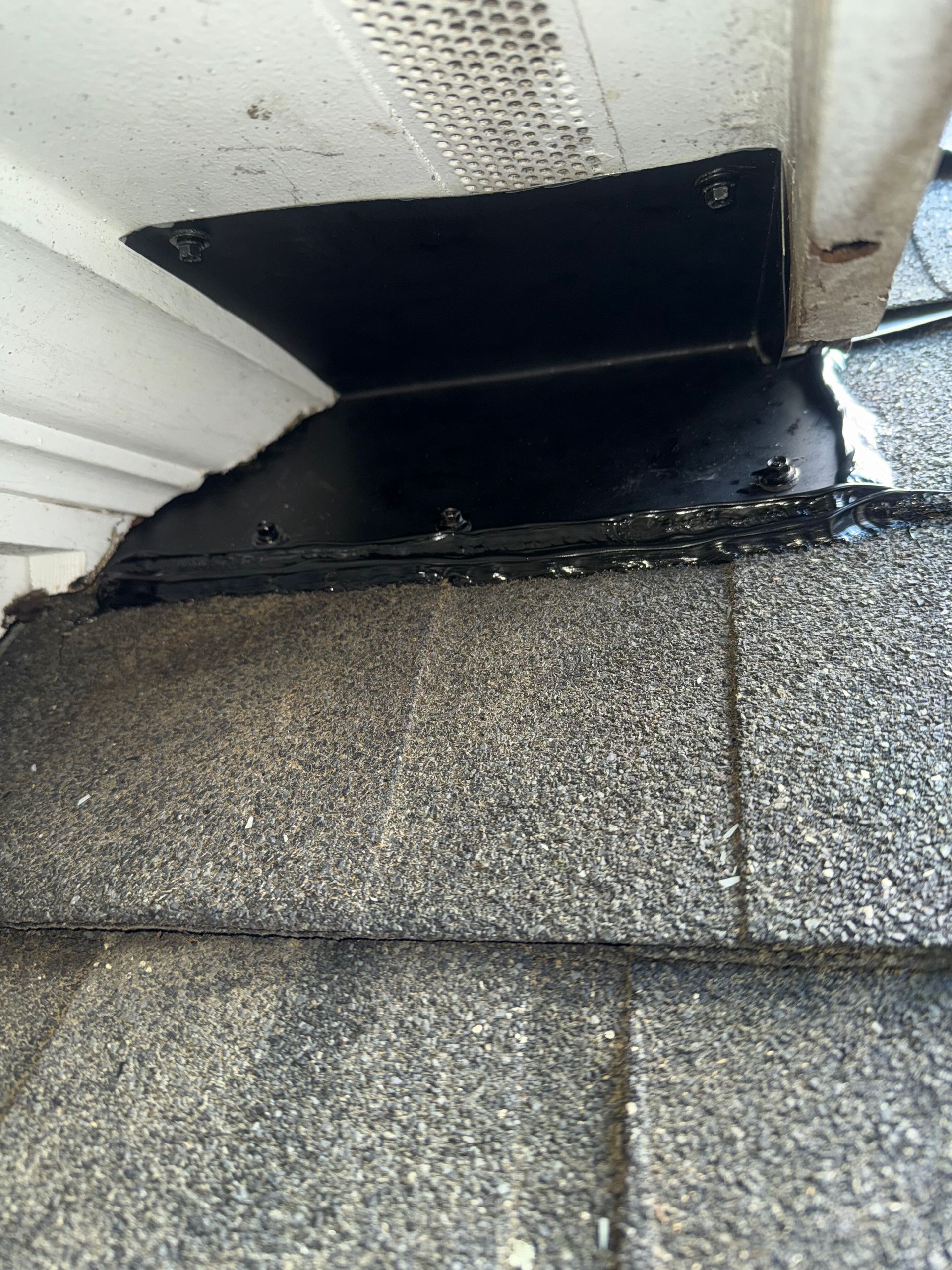 Black flashing around a roof vent where the siding meets gray shingle roofing.