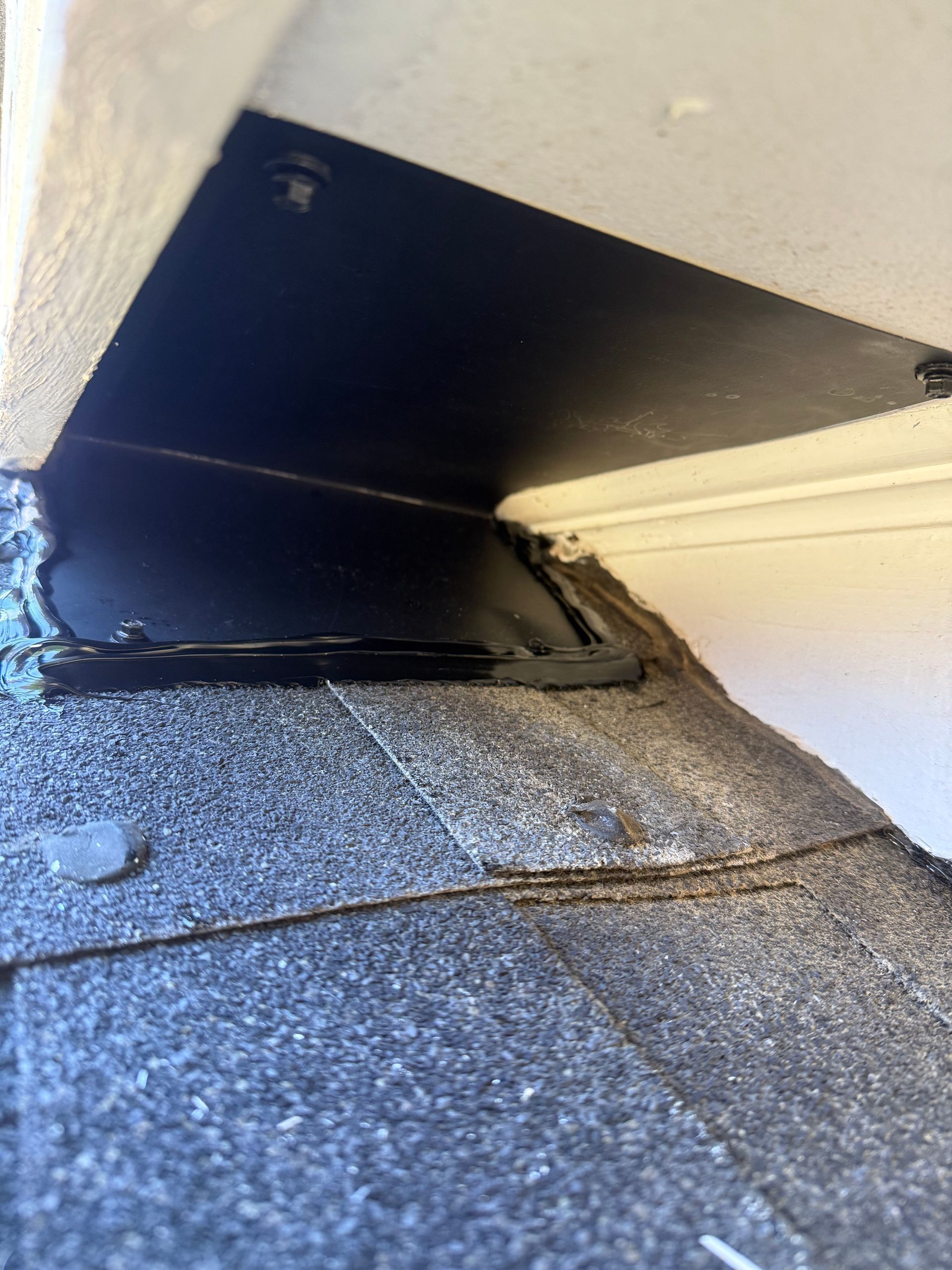 Damaged roof flashing at a wall corner, with peeling sealant and asphalt shingles below