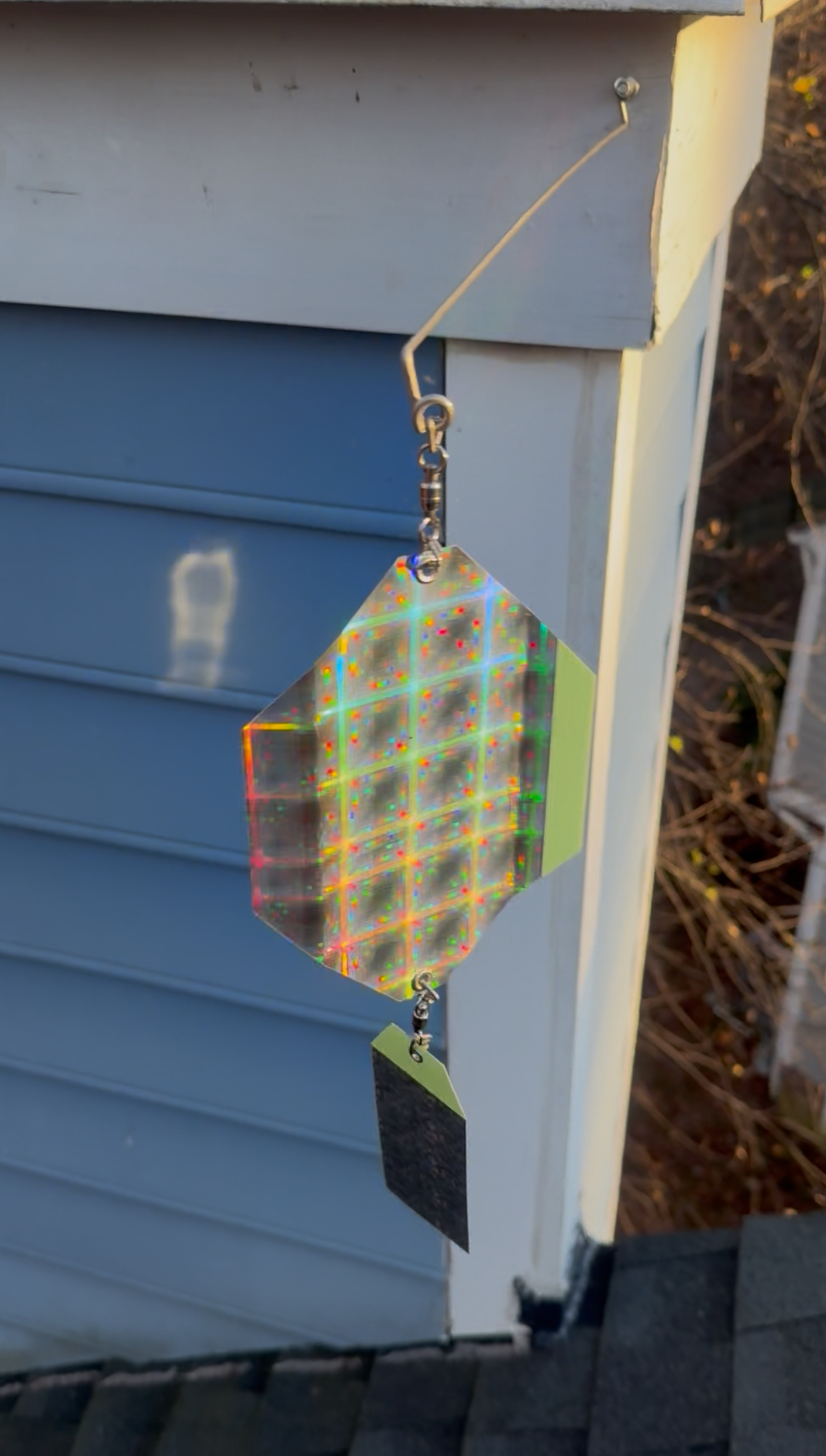 Plaid wind spinner hanging from a hook on a house corner by gray siding and a white trim board