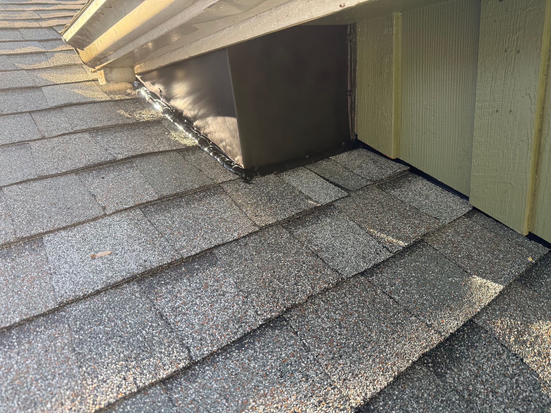 Rooftop shingles beside a dormer wall with exposed flashing and roof edges