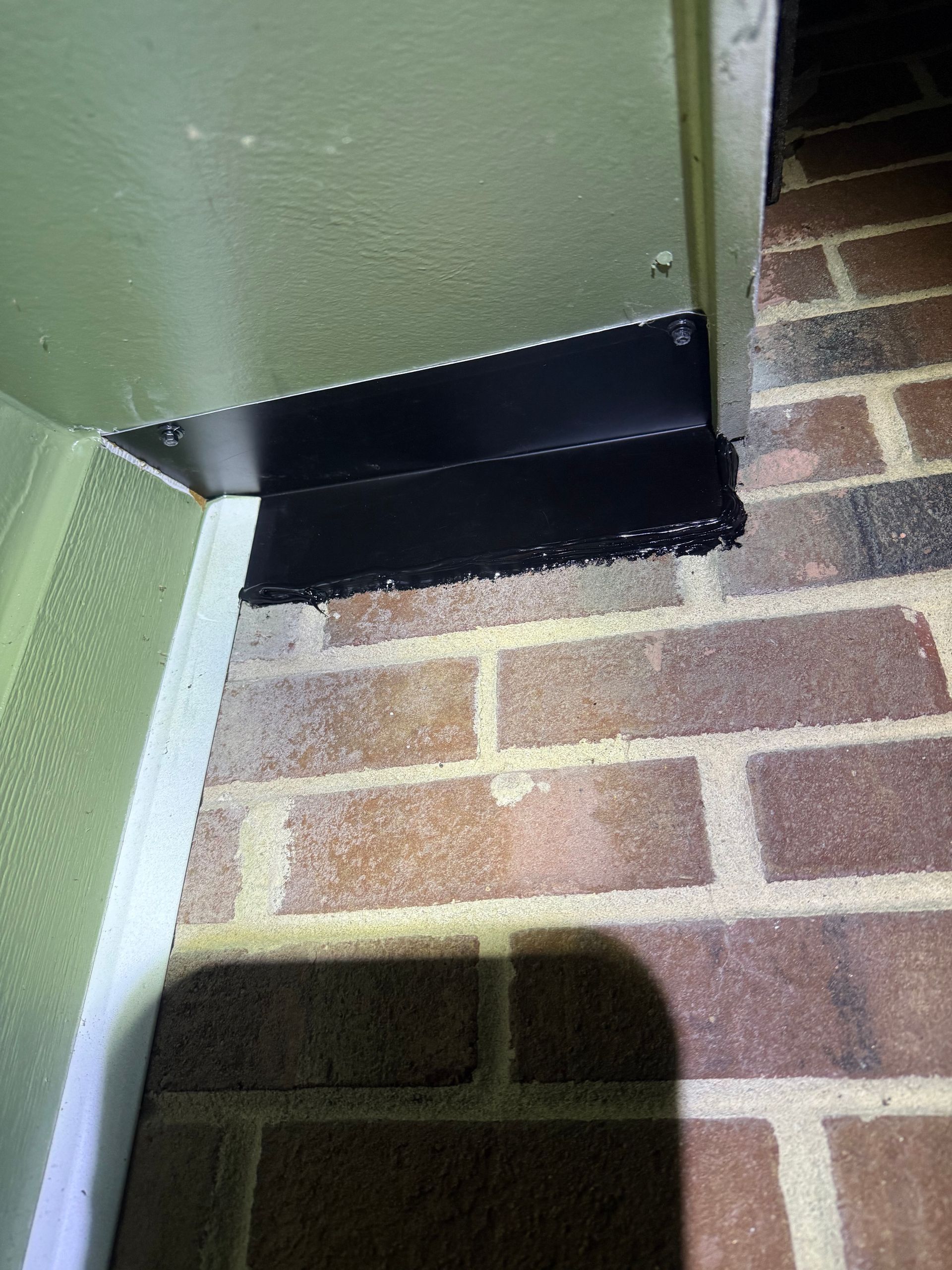 Green exterior wall with black metal corner trim above a brick patio.