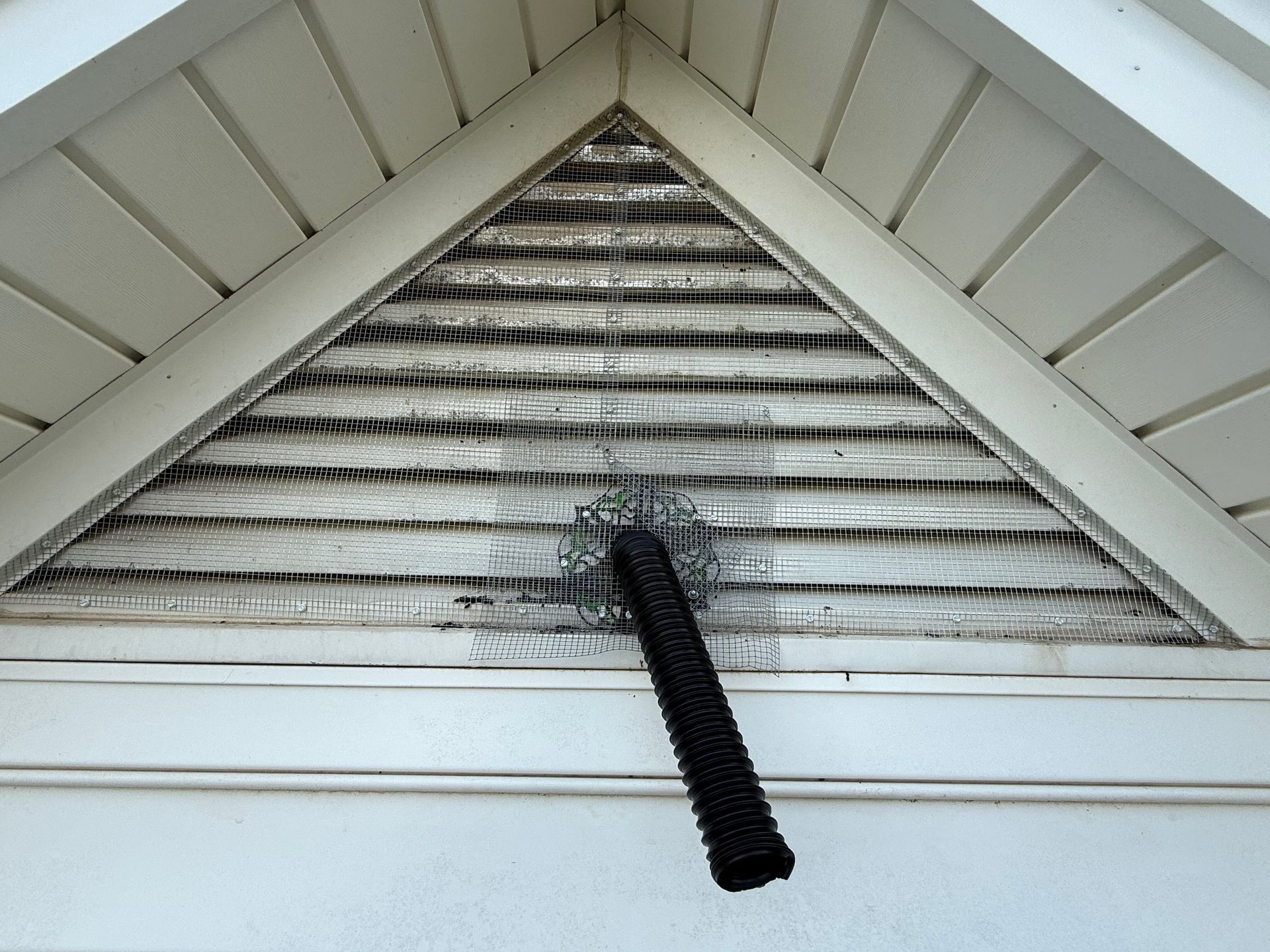 Attic gable vent with weathered white slats and a black brush-like rod hanging down