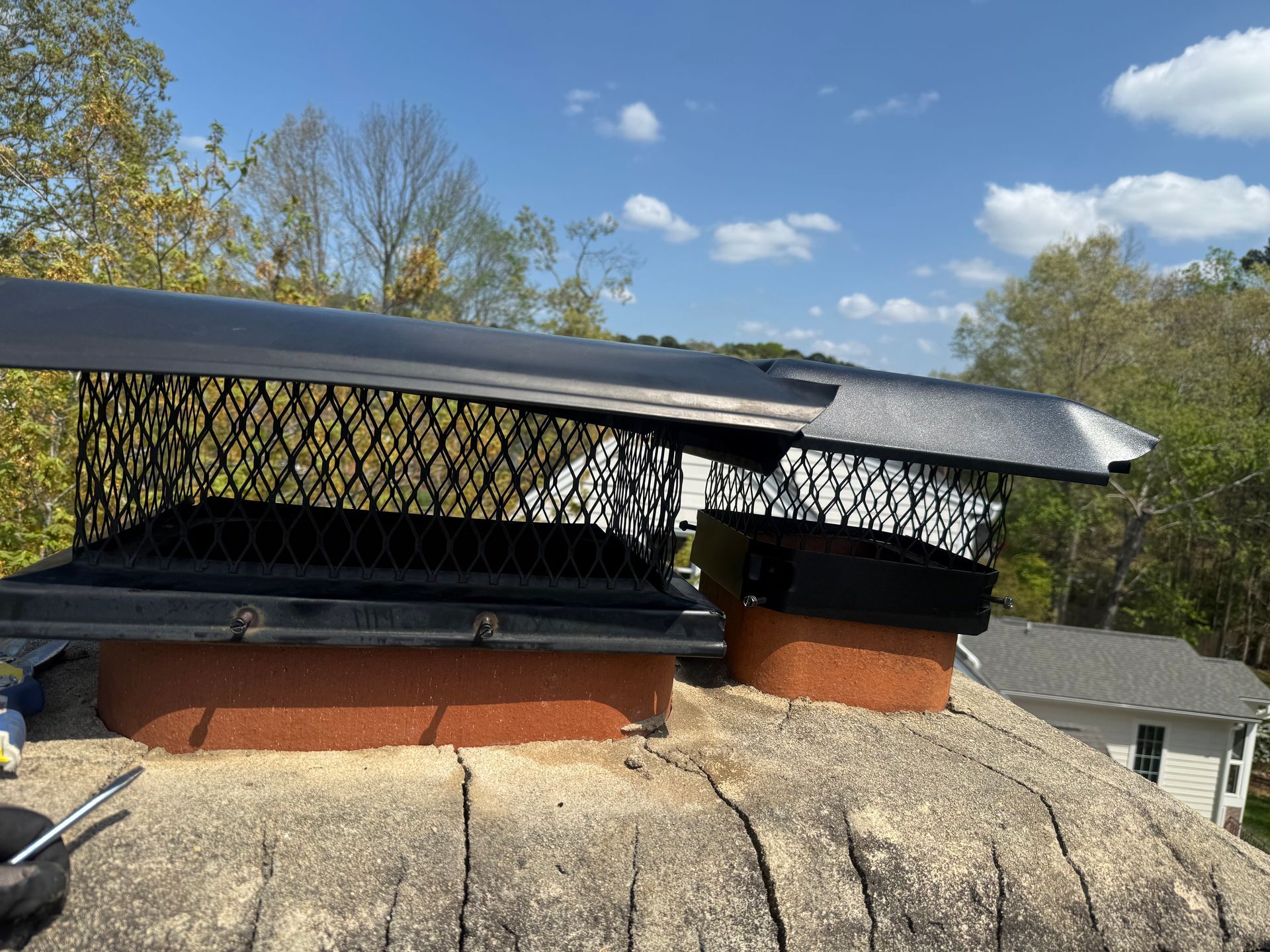 Two black chimney caps on a shingled roof under a blue sky