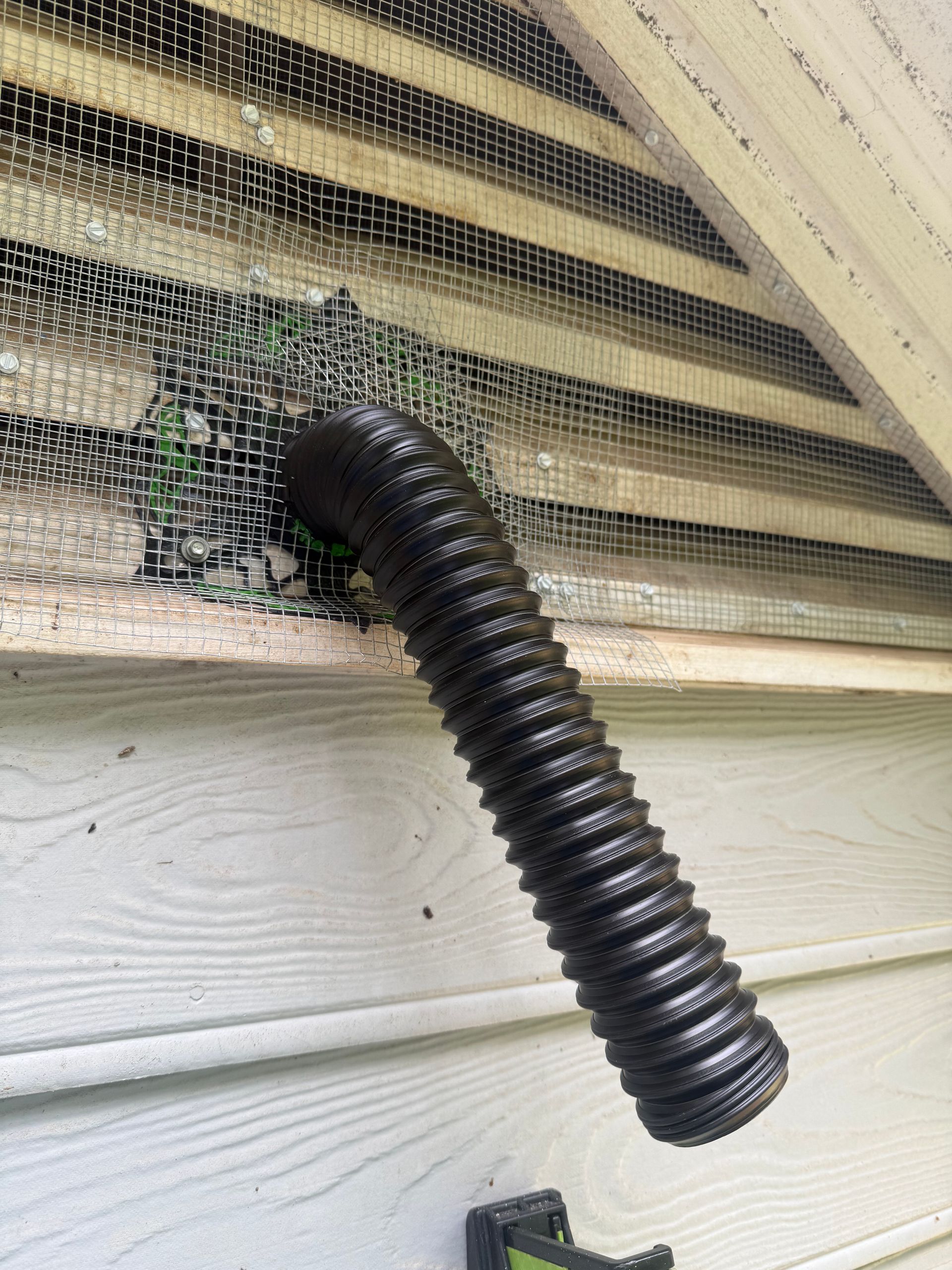 Black corrugated hose extending through a window screen with a torn opening.