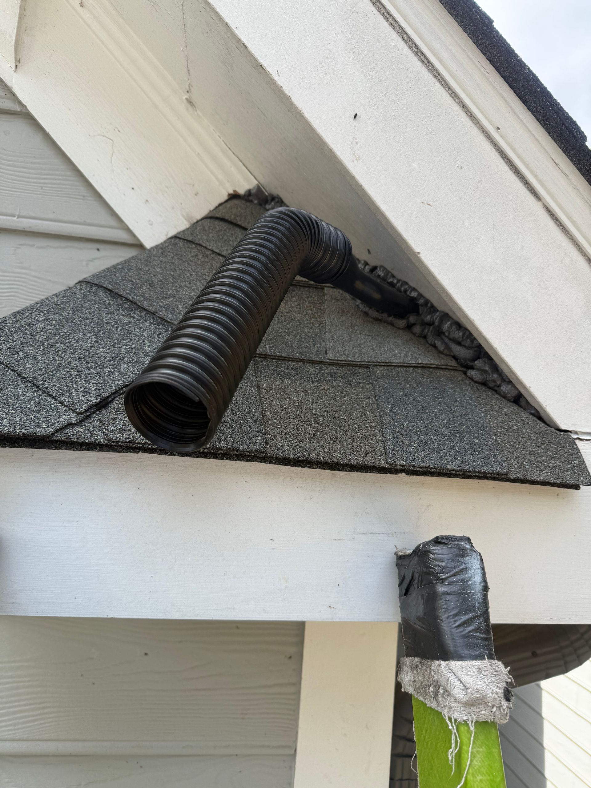 Black corrugated hose on a roof vent beside a smaller duct wrapped in silver tape