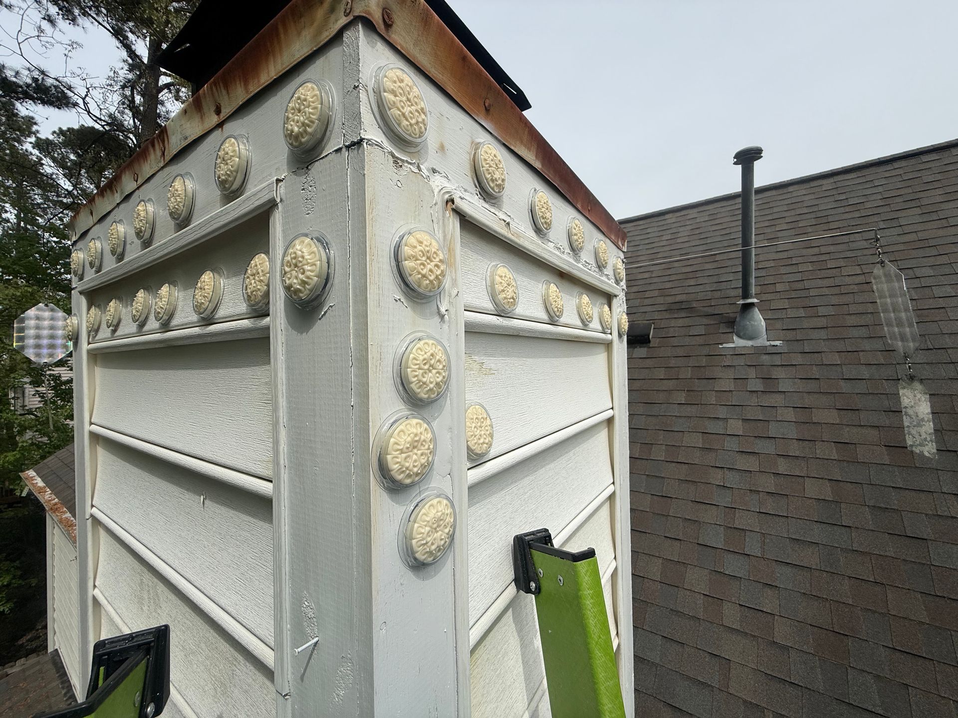 Rooftop metal chimney with white panels, beige decorative studs, and a dark shingled roof in the background