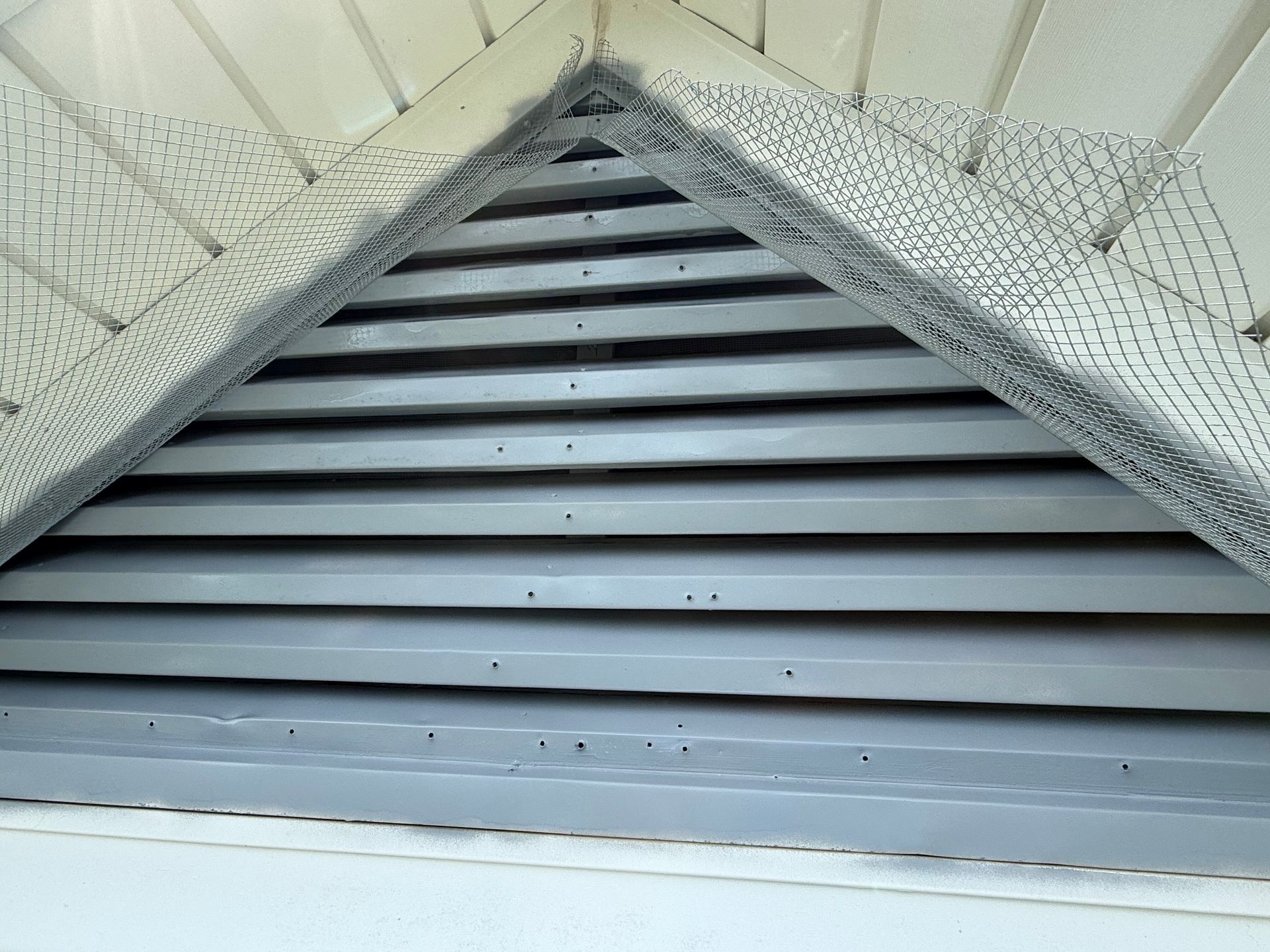 Close-up of a gray louvered vent set in a triangular wall opening above white siding.