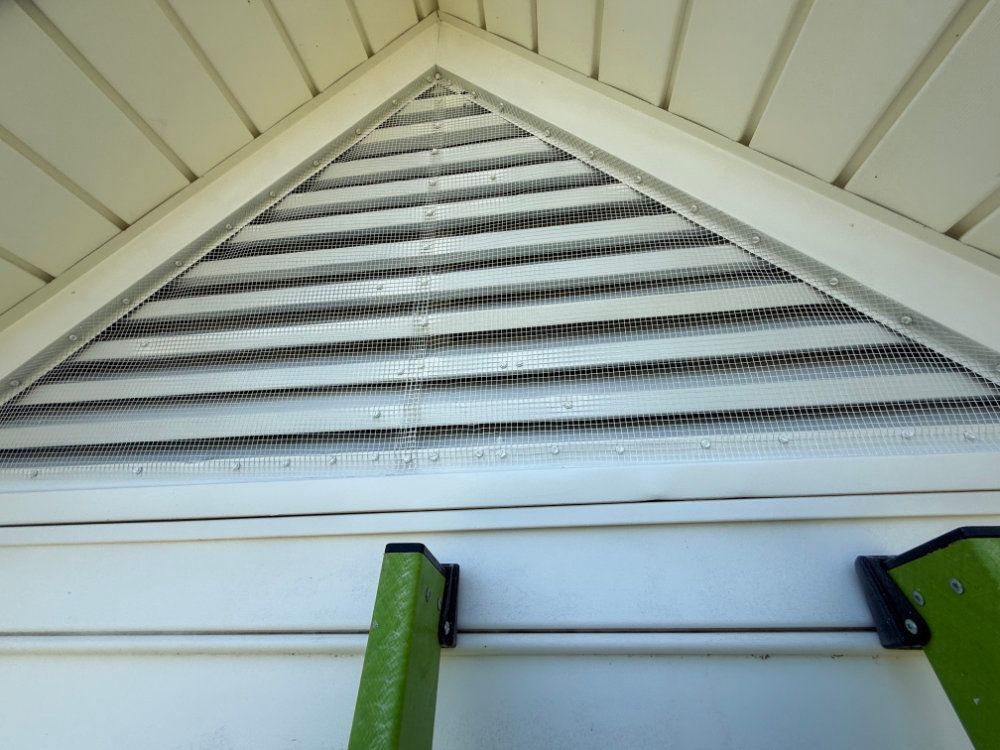 White gable vent with horizontal slats and green brackets on an exterior wall