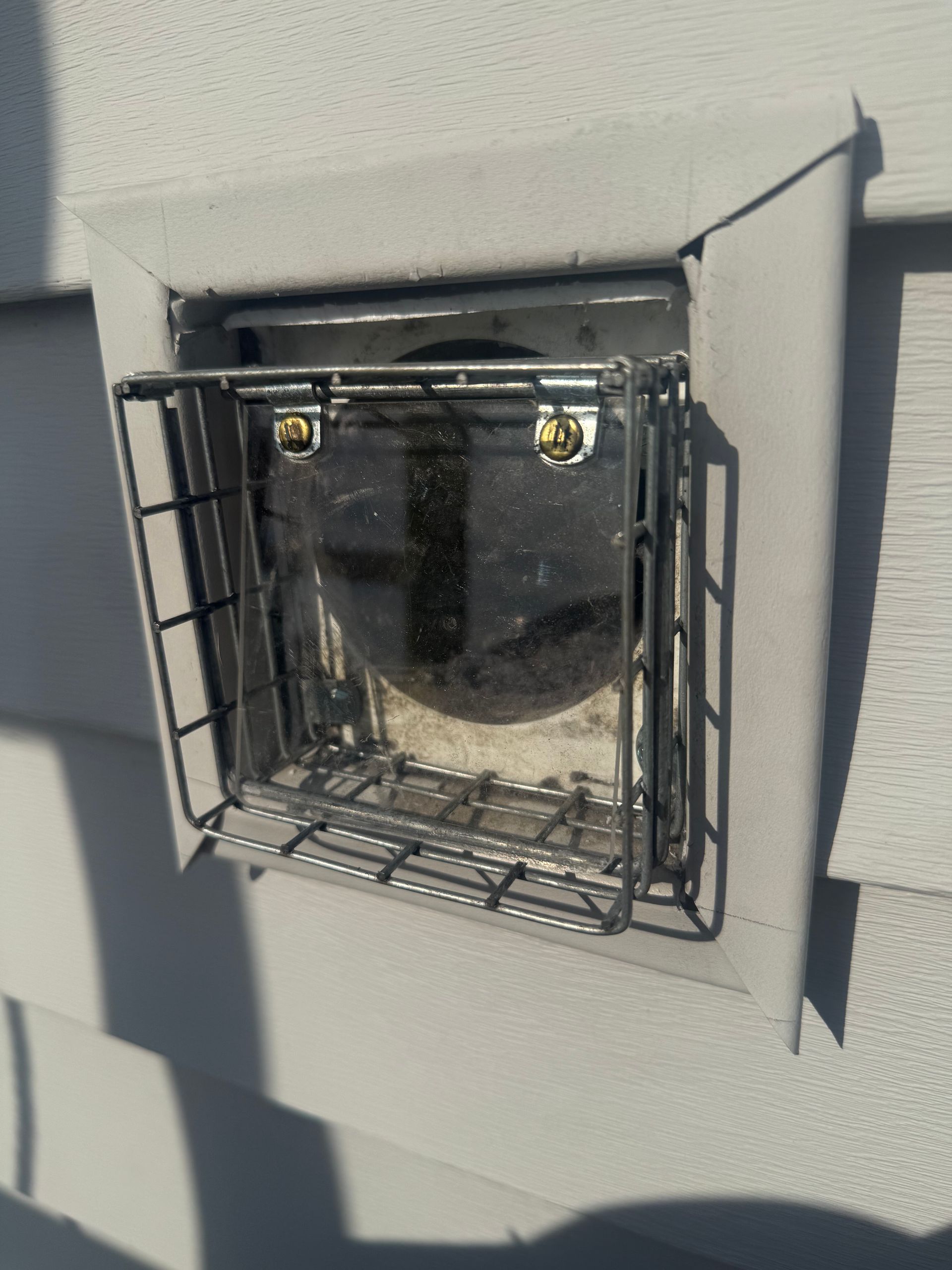 Open wall vent with black metal cage on a gray exterior wall