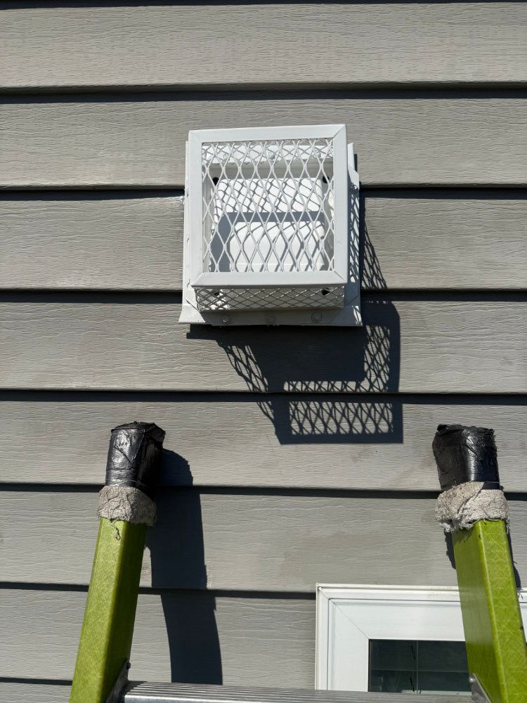 White wall-mounted outdoor light casting shadow on gray house siding beside two green ladder tops