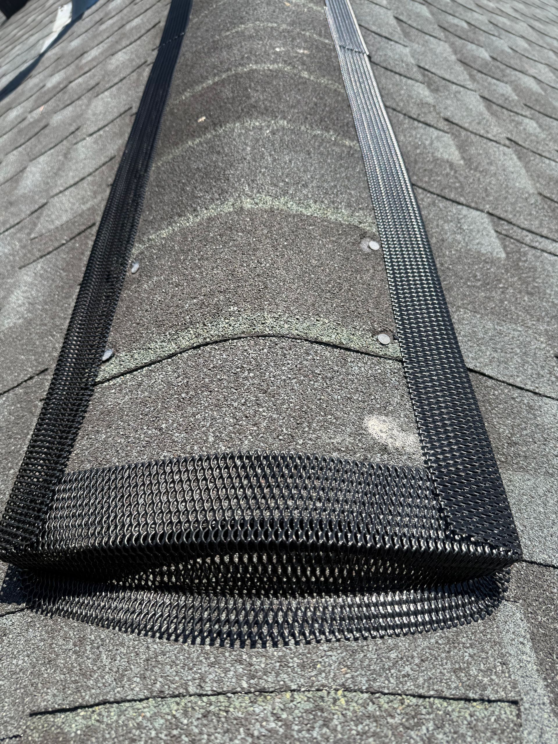 Rolled-up roof shingle bundle on a gray shingled rooftop