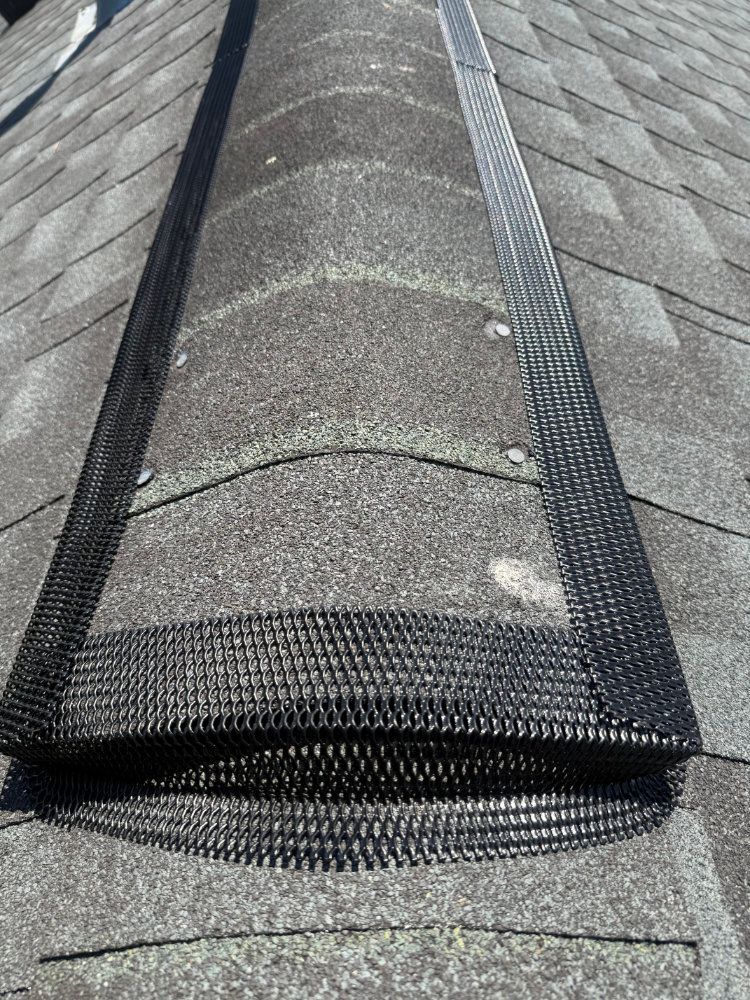 Rolled roofing underlayment on a shingled roof, with a loose section lifted near the ridge.