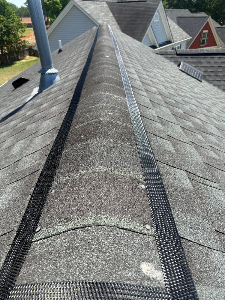 Roof ridge with gray shingles and black ventilation strips on a house roof