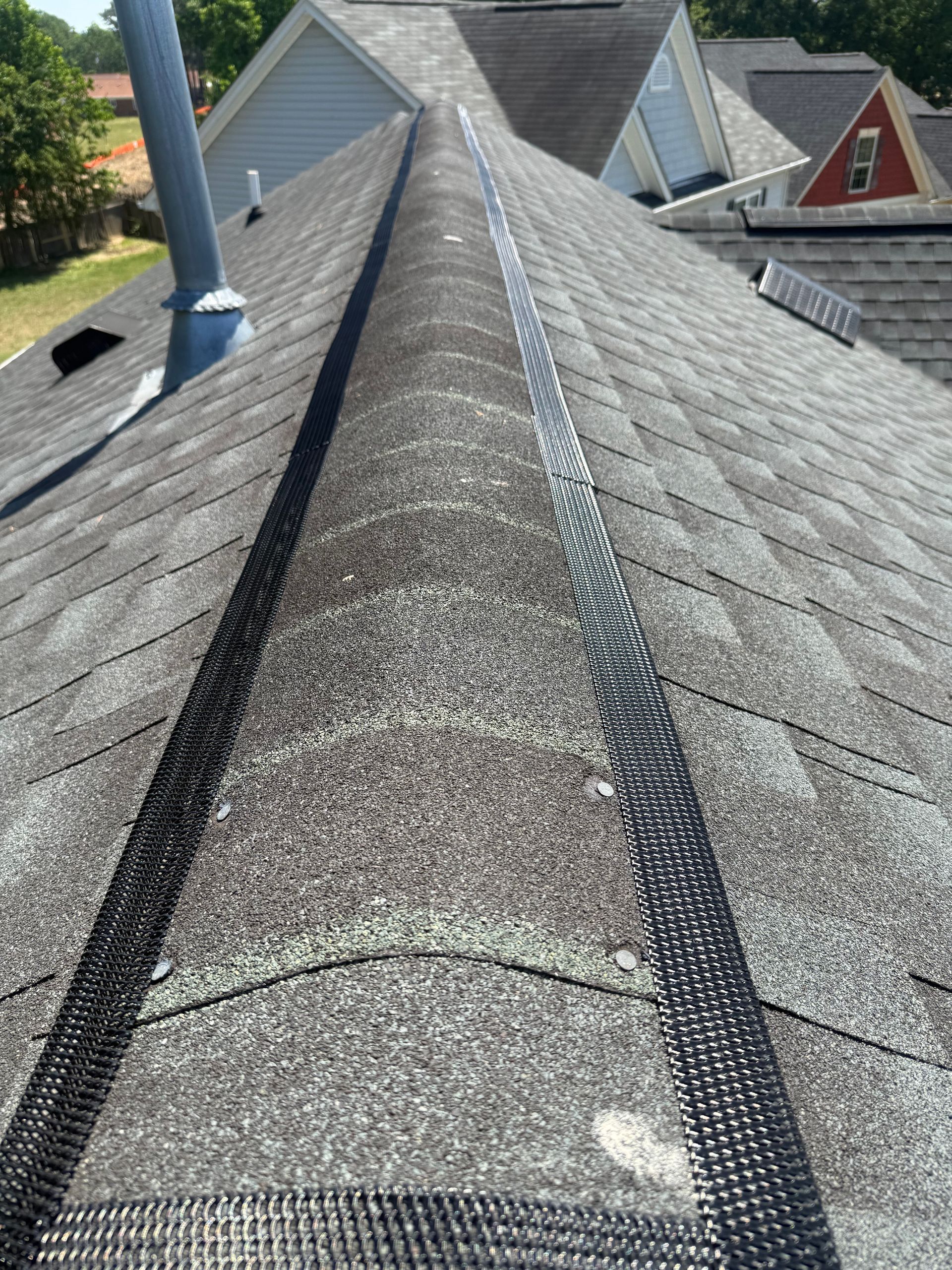 Shingled house roof ridge with black vent strips and neighboring rooftops visible
