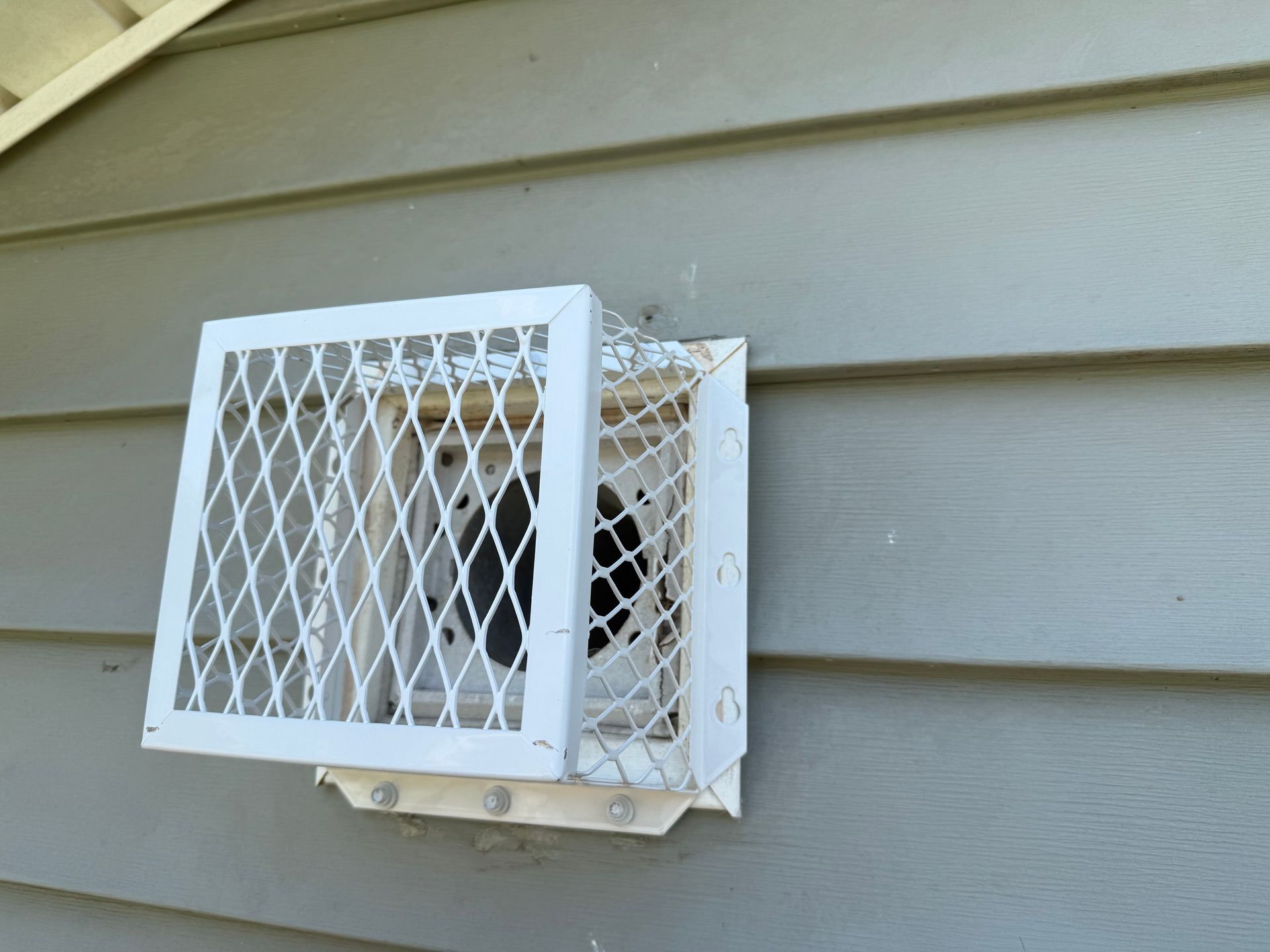 White metal box mounted on beige siding, with a diamond-mesh cover and open front panel