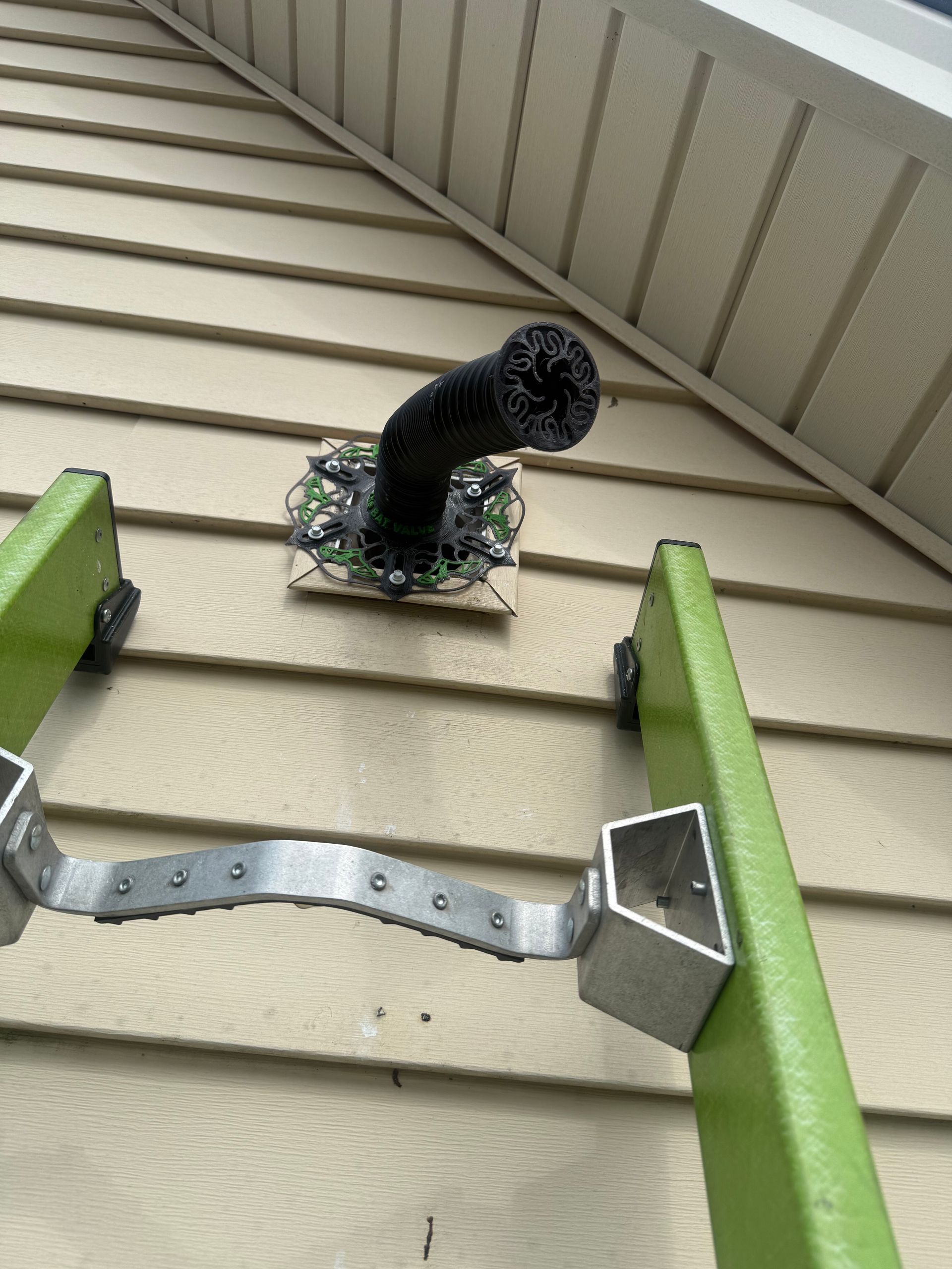 Black vent pipe protruding from tan house siding, with ladders visible below on both sides.