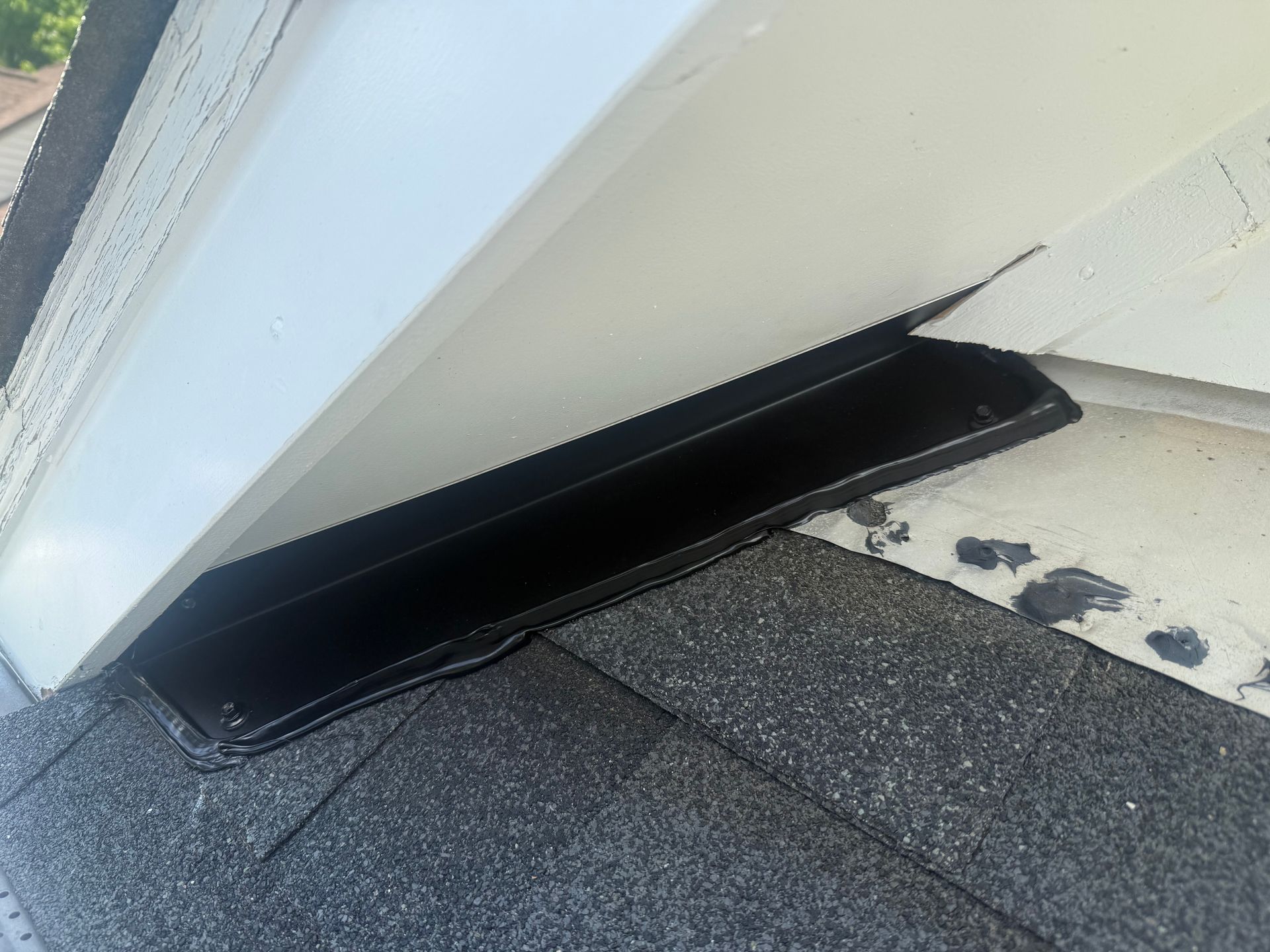 Black roof vent protruding from a white wall above gray shingles near a roof edge