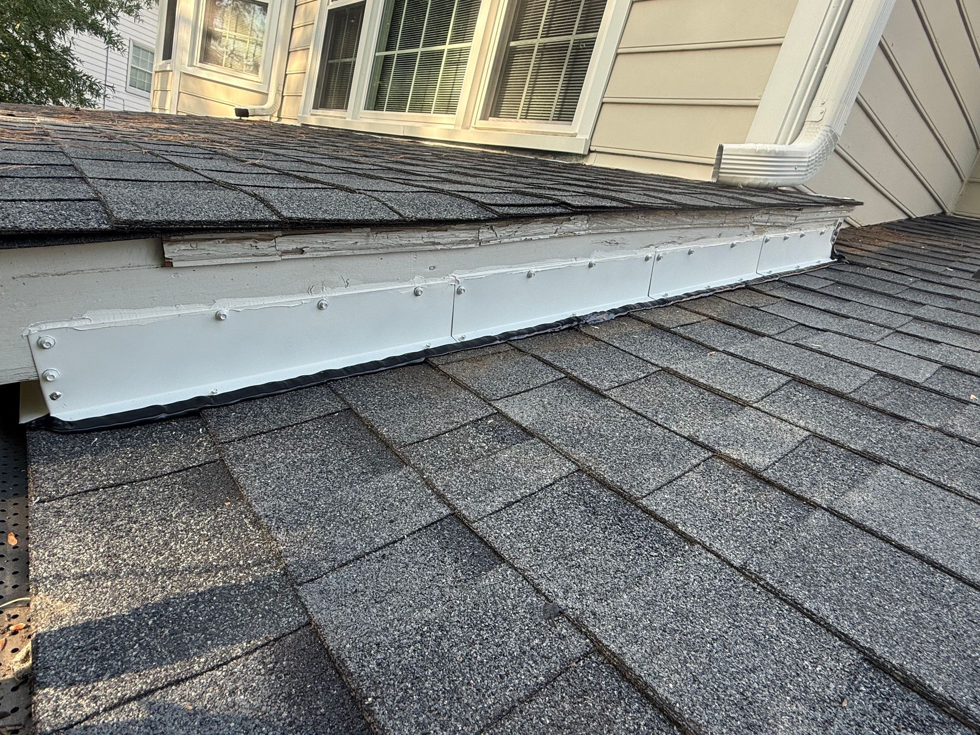 White metal roof flashing lifted over gray shingle roof near a house window