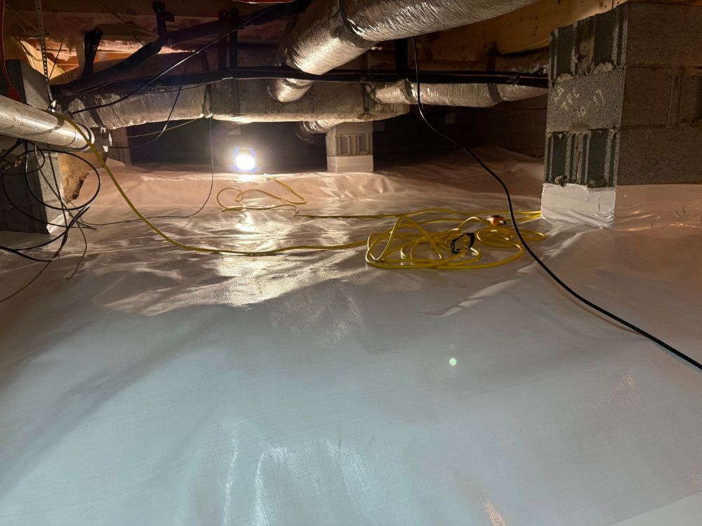 Crawlspace with plastic vapor barrier, exposed ducts, wiring, and a bright work light overhead