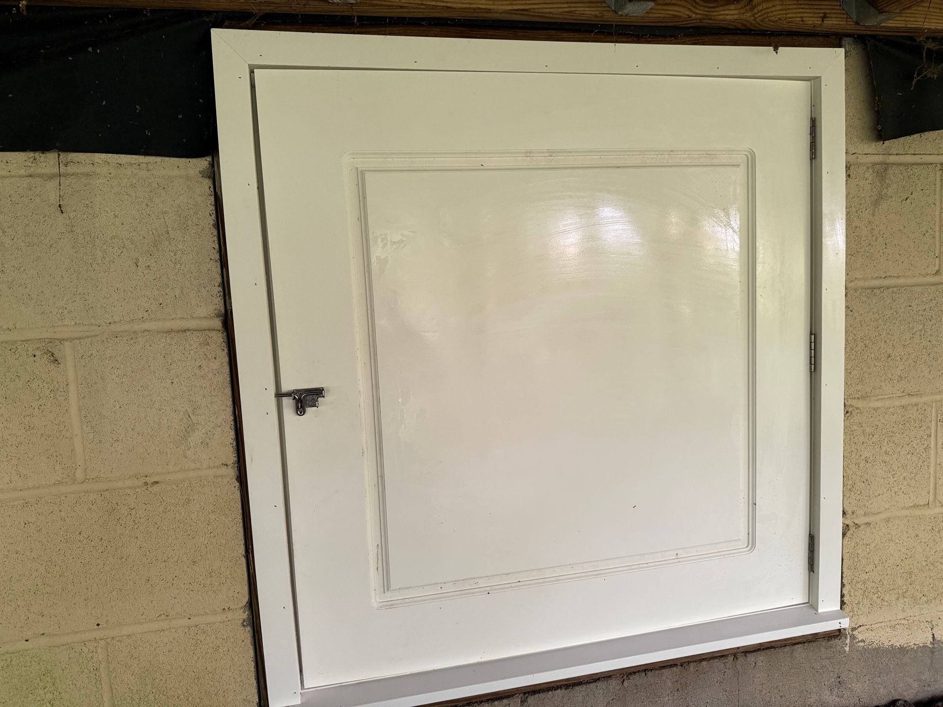 White utility door set into a beige cinder block wall, with a small handle and slanted base