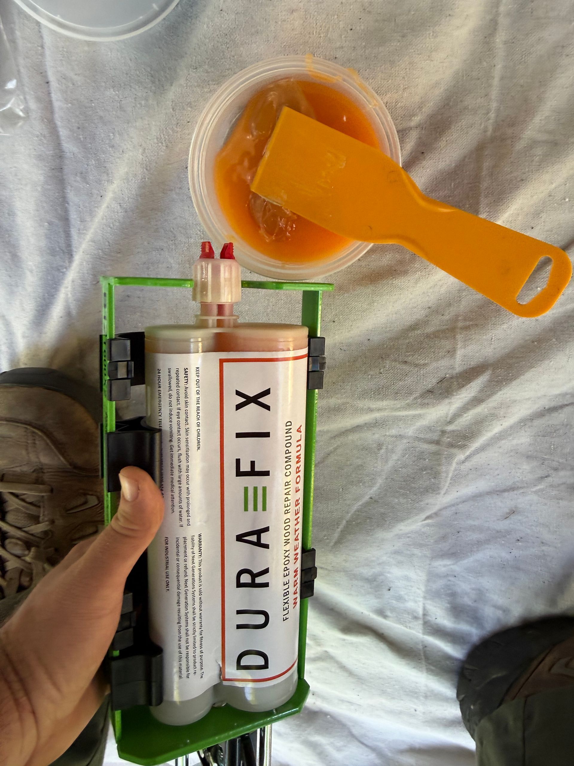 Hand holding a small 3D-printed device with a tube and orange liquid in a cup on a gray cloth.