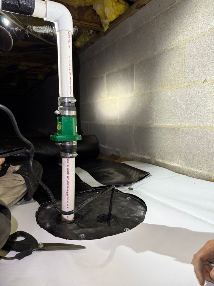 Basement utility area with white PVC pipes, black waterproofing around floor penetrations, and cinderblock wall