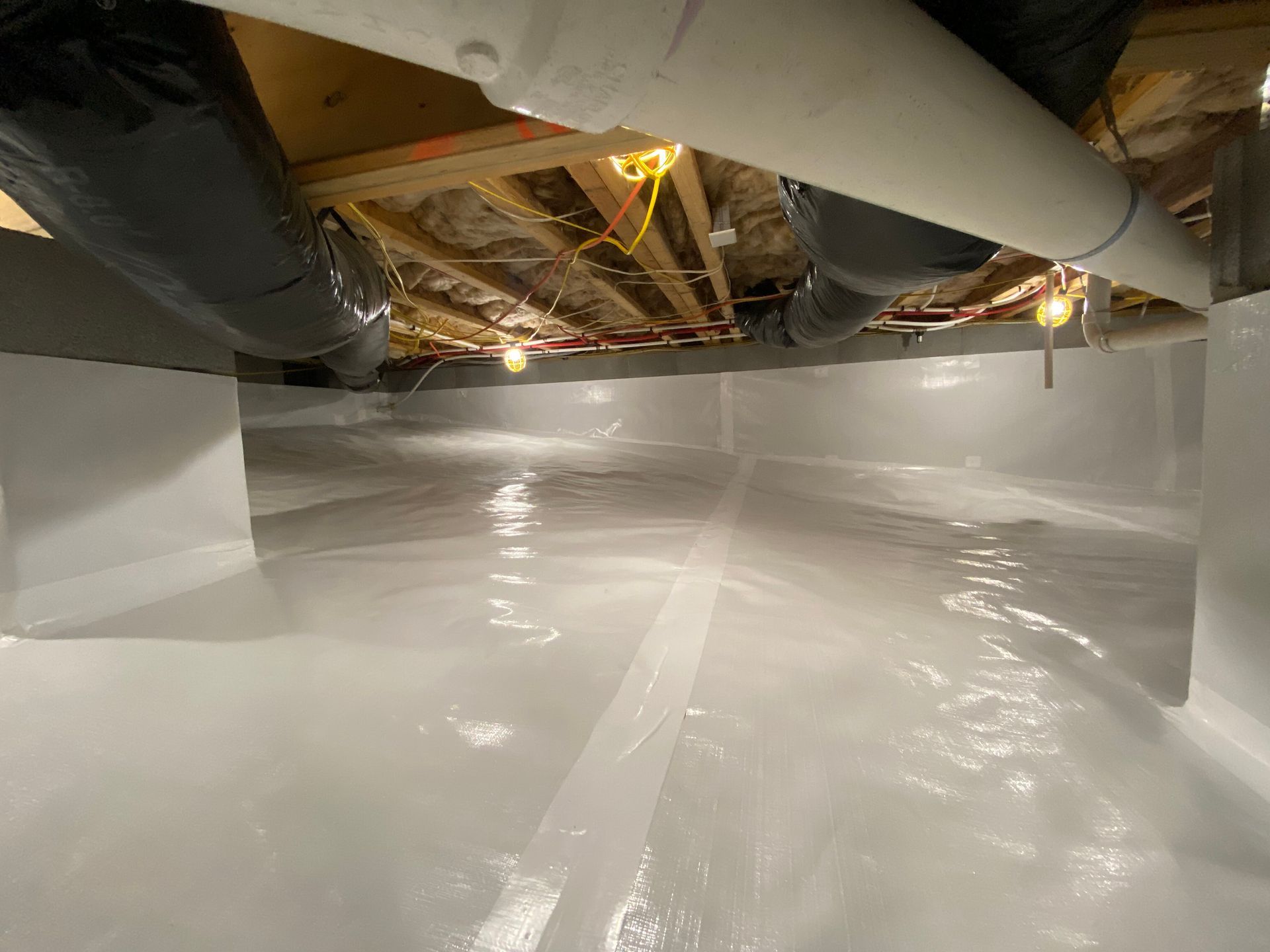 Basement crawlspace with white vapor barrier floor, exposed pipes, ducting, and ceiling joists.