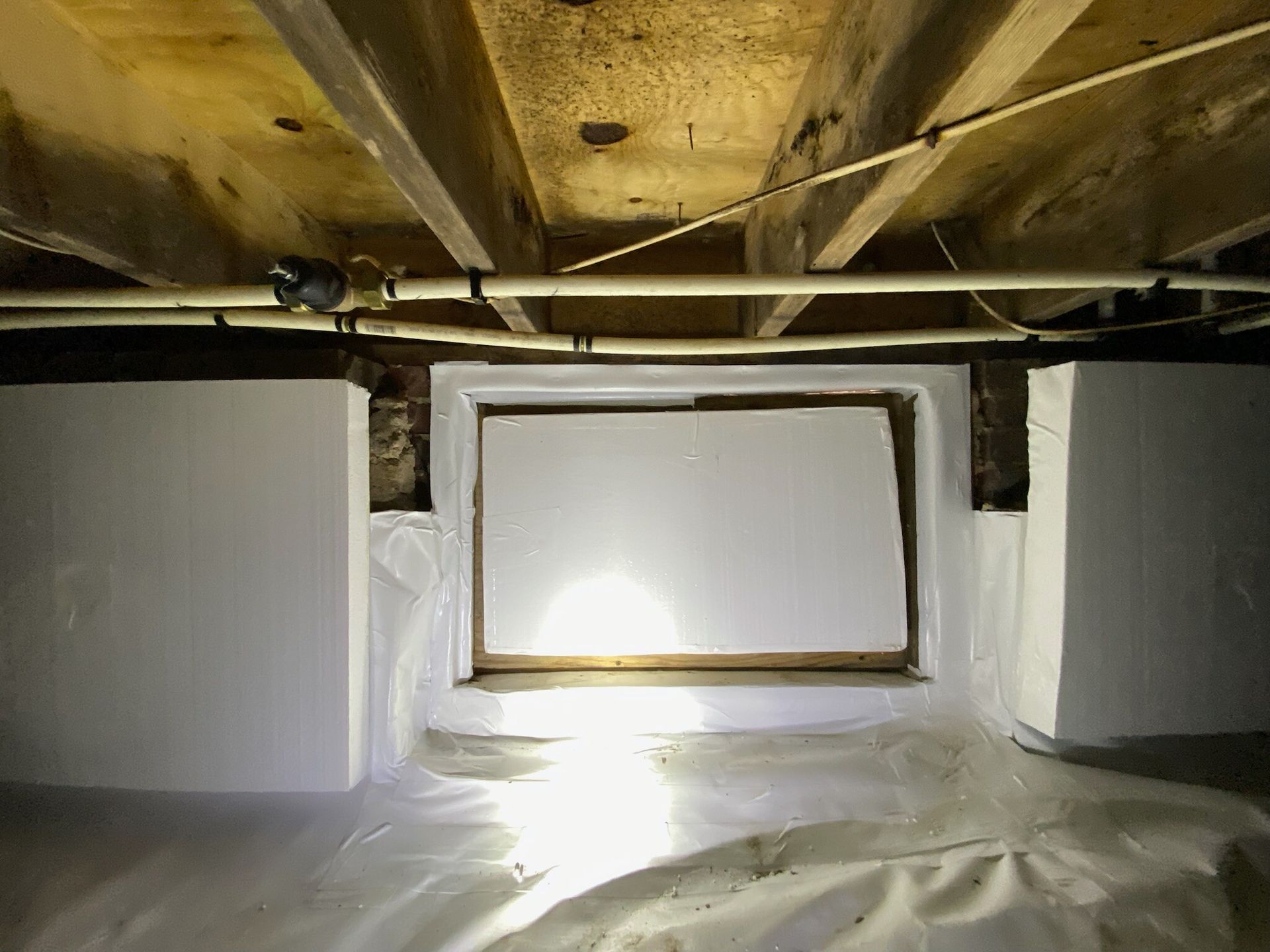 Insulated crawl space with exposed wooden beams and a small vent opening in the foundation wall