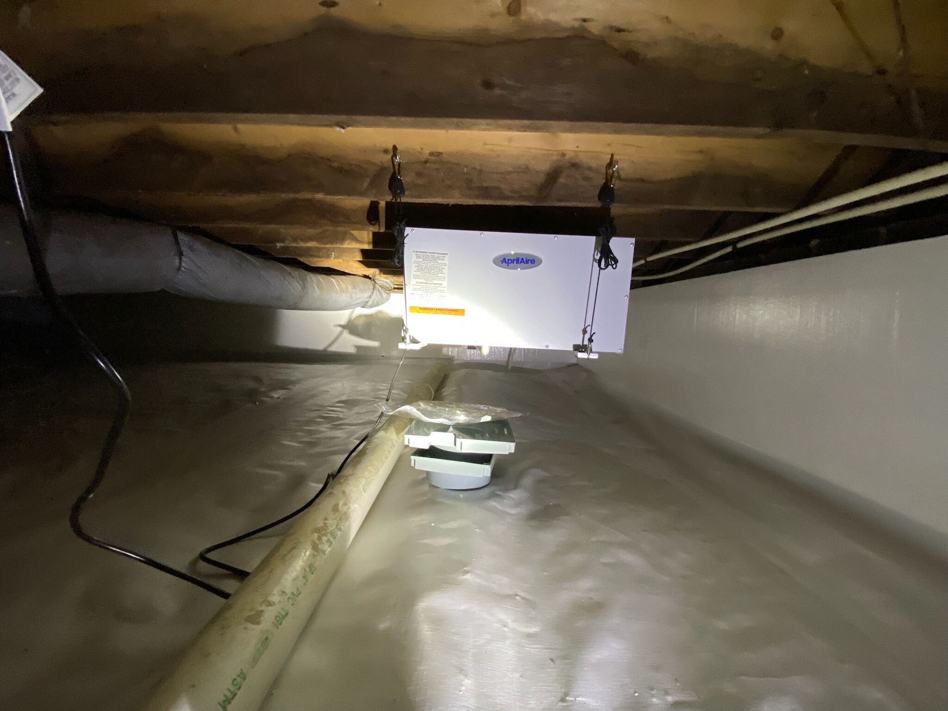 Dim crawlspace with ductwork, a white unit, and a light illuminating the low ceiling.