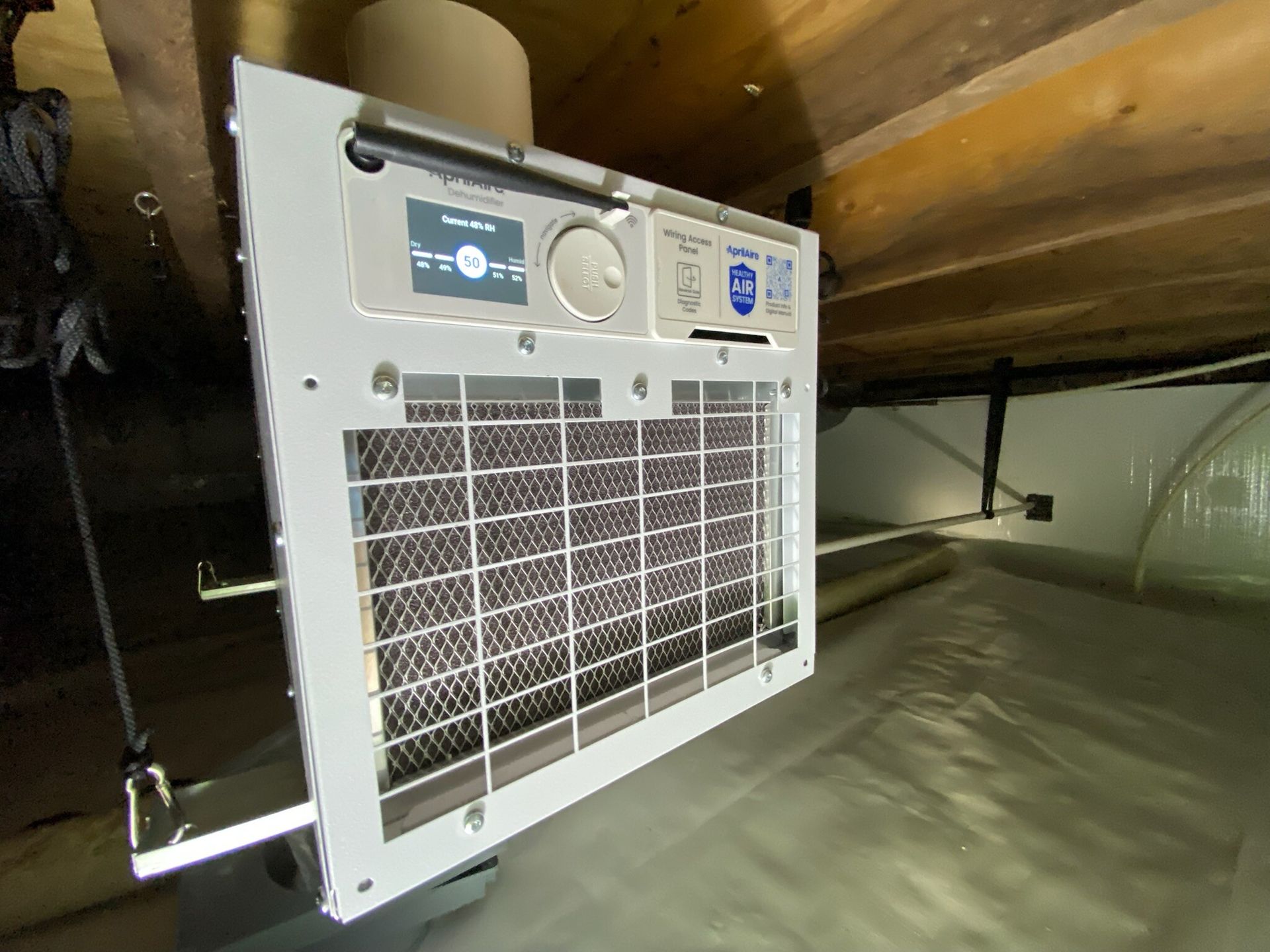 Portable air conditioner mounted in a crawlspace, with white casing and front grille.