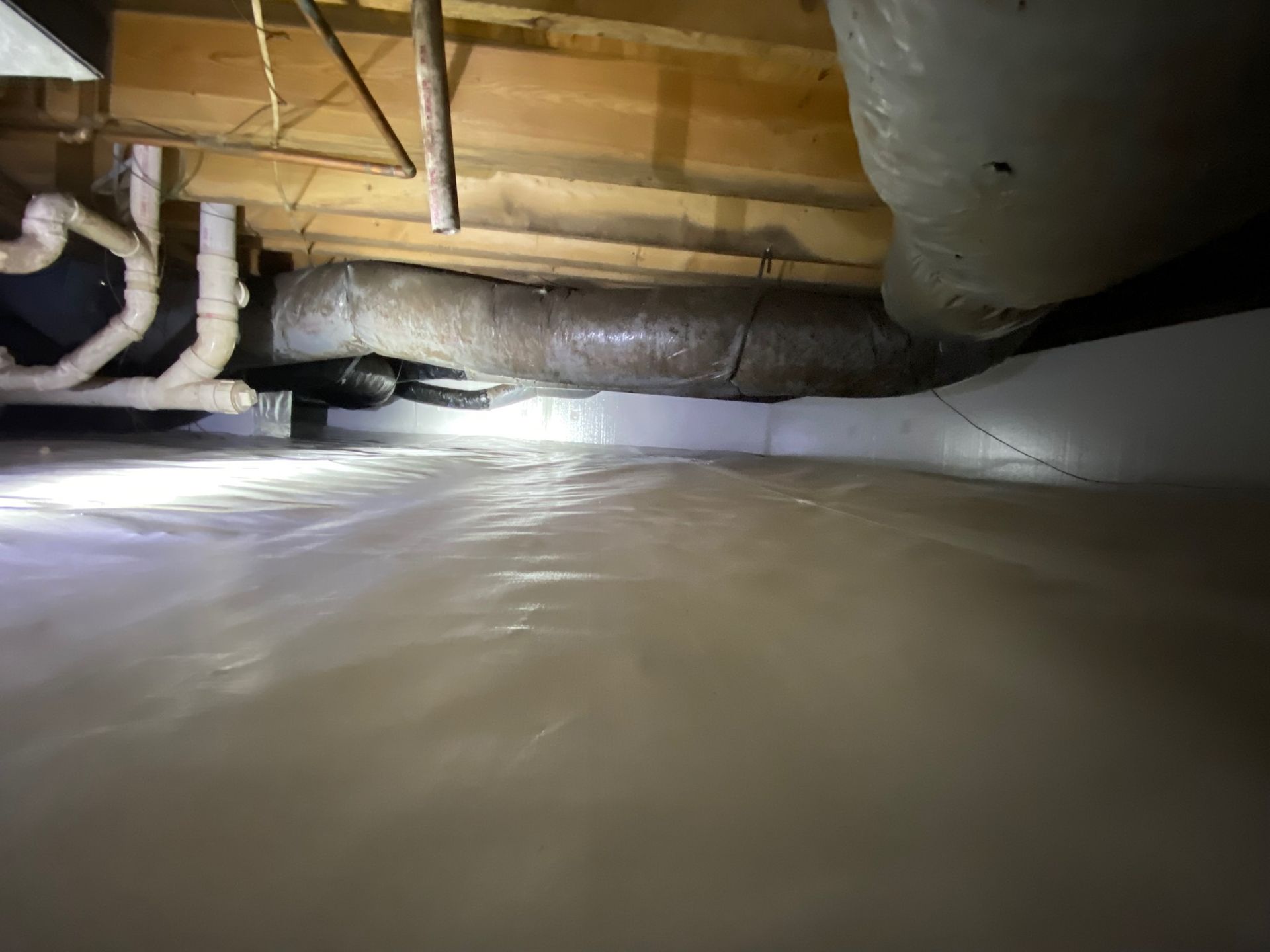 Flooded crawl space under a house, with standing water, pipes, and exposed wooden beams.