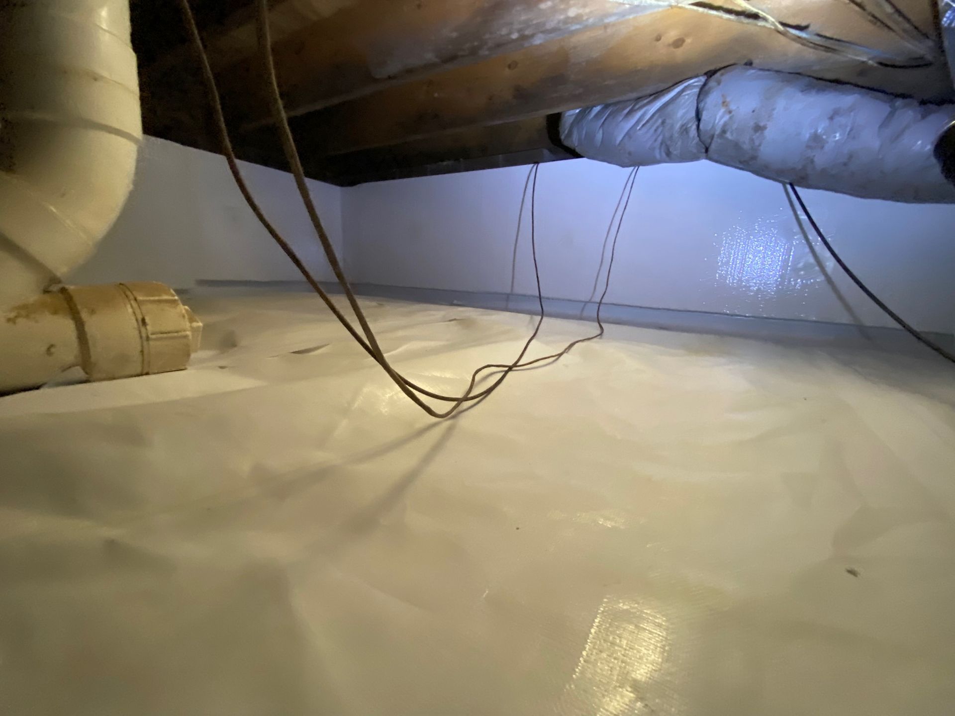 Insulated attic crawlspace with hanging cables and a glossy white floor lining