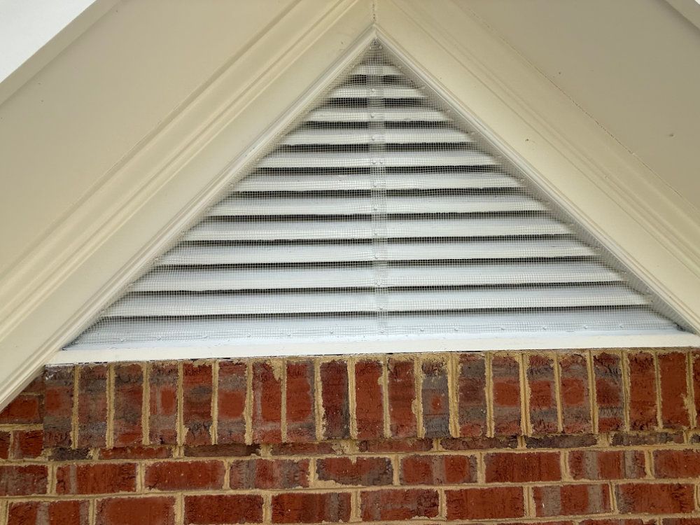 Triangular attic vent with white louvered slats above a red brick wall