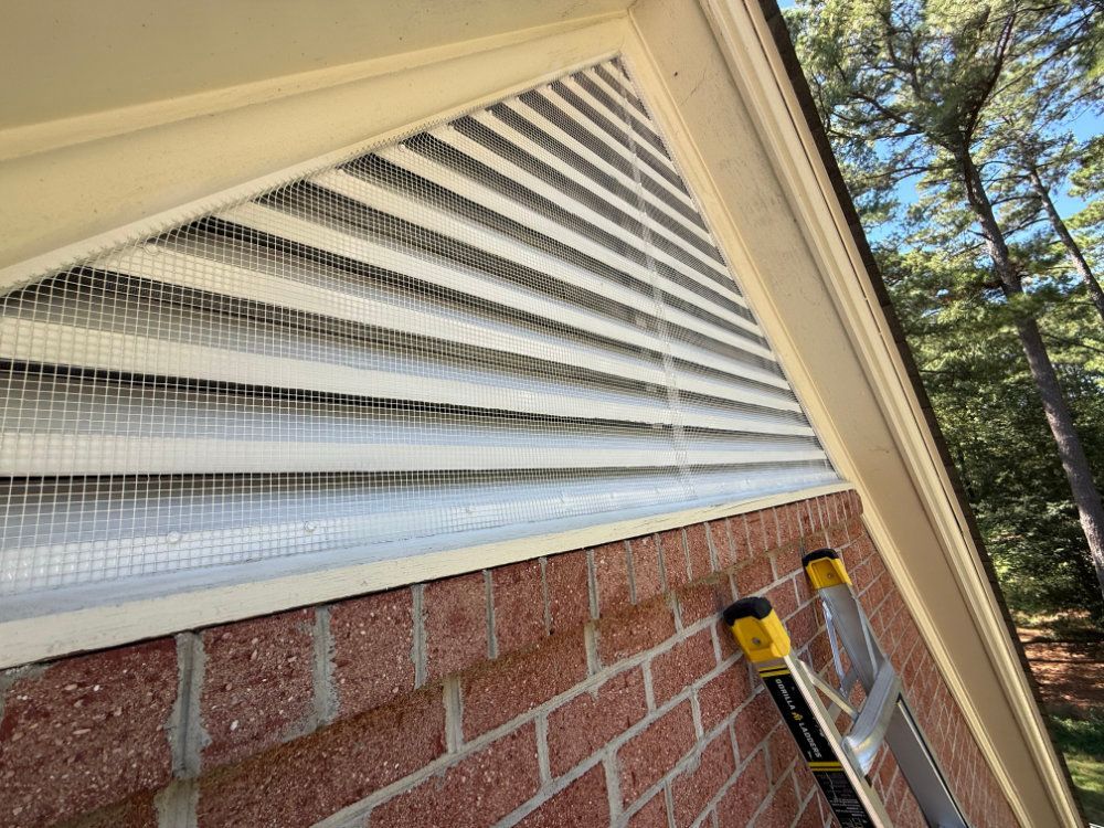 White louvered vent under eaves on a brick house, with a yellow drill and ladder beside it