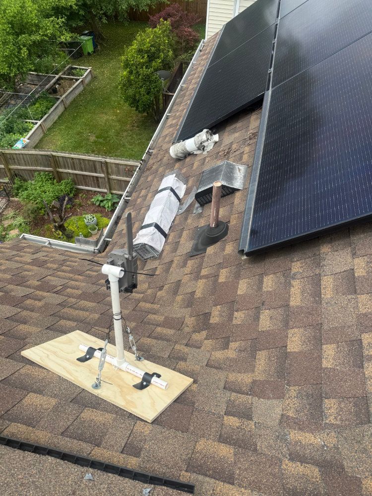 Rooftop with solar panels, a small antenna, and a partially open roof hatch near the shingles