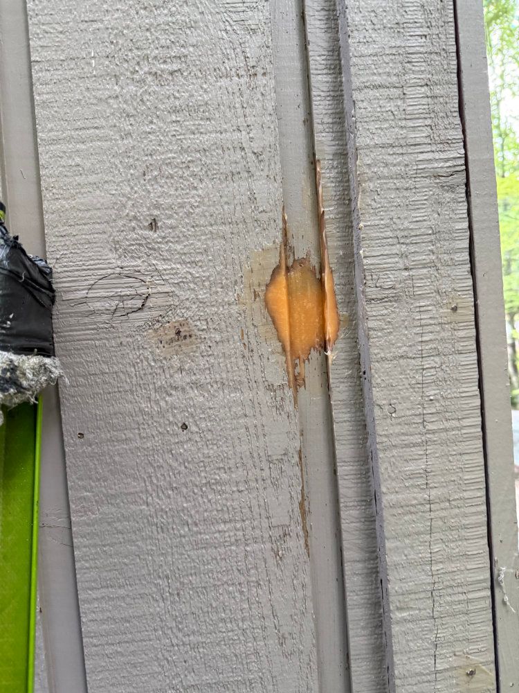 Close-up of a gray wooden fence with a chipped orange-painted area and visible cracks.