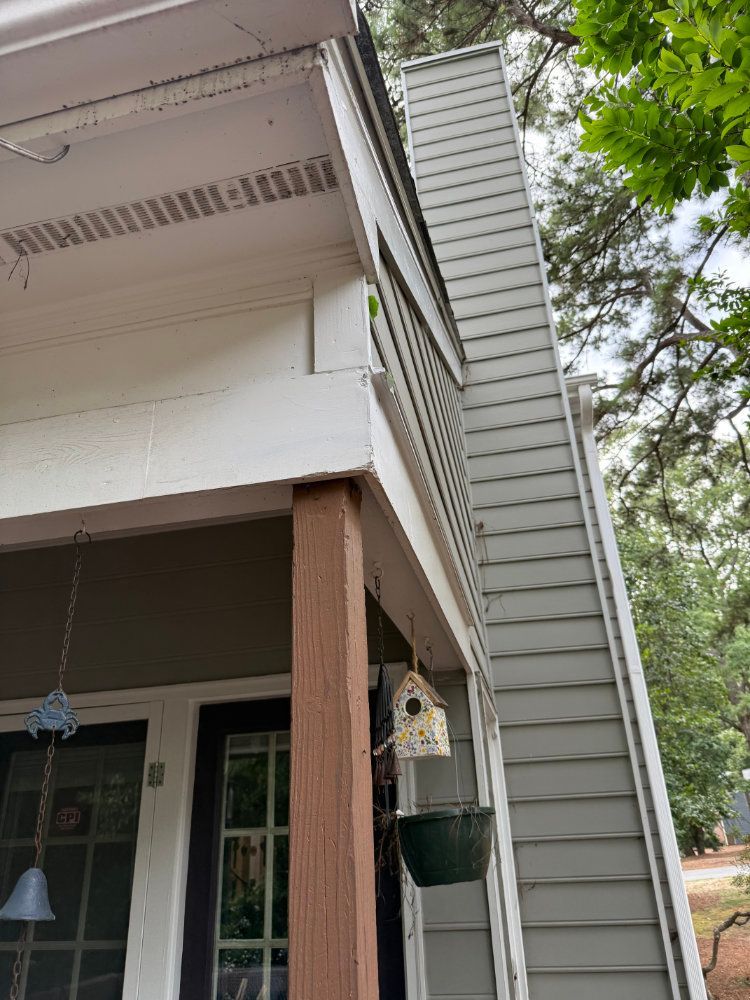 Front porch with white siding, wooden post, hanging bird feeder, and trees in the background