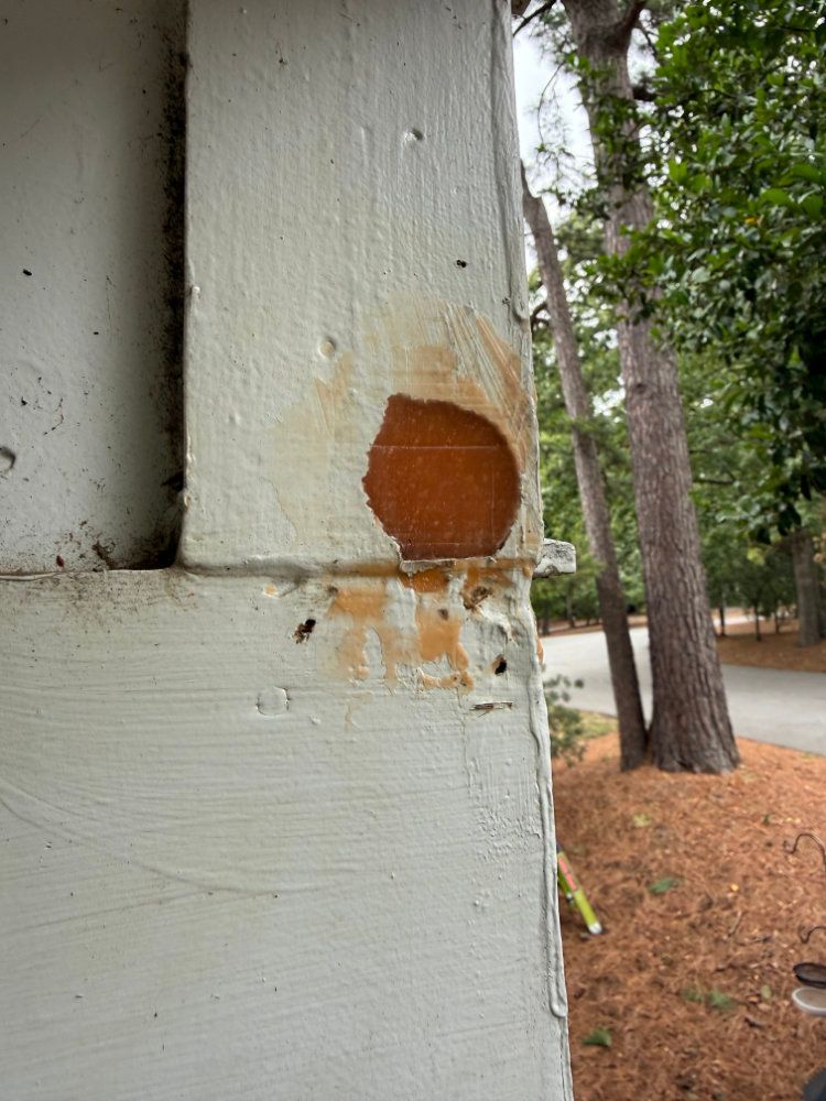 Close-up of weathered white siding with a rust-colored patch and chipped paint near a corner outdoors