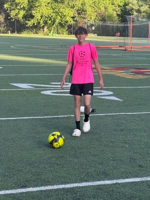 Teenager in pink shirt and black shorts with a soccer ball on a green field.