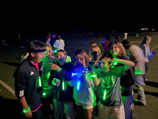Group of people wearing glow sticks at night, smiling and making hand gestures on a field.