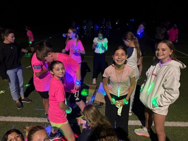 Group of girls wearing pink and green glow sticks, smiling outdoors at night.