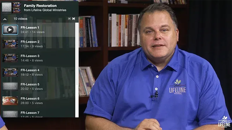 A man in a blue polo shirt sits in front of a bookshelf next to a video playlist titled 