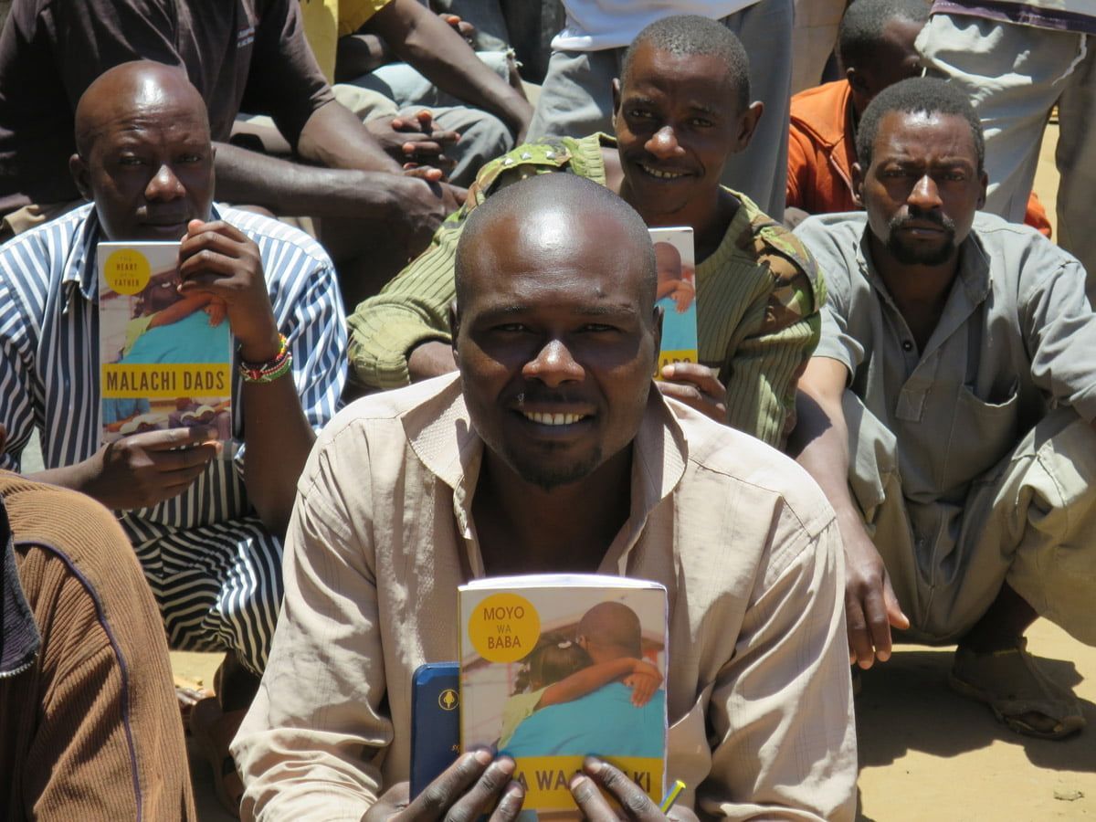 Several people seated outdoors hold up copies of the same book featuring a yellow circular emblem on the cover.